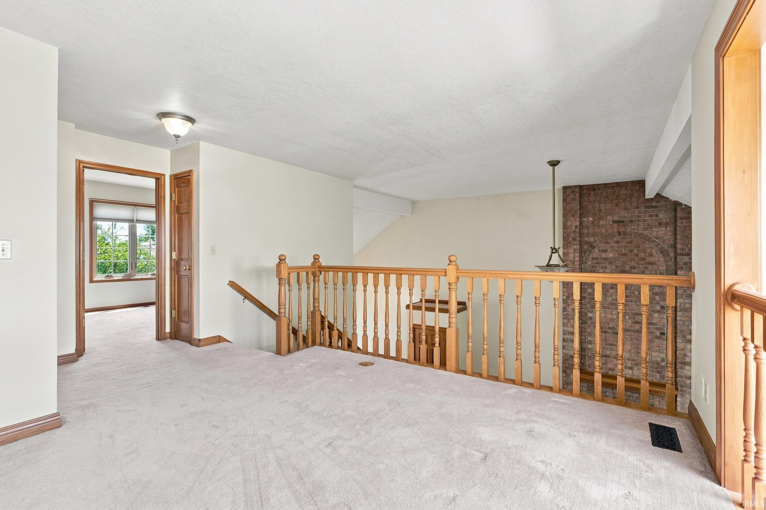 Carpeted upstairs landing featuring a wood banister, brick accent wall, and a built-in light fixture