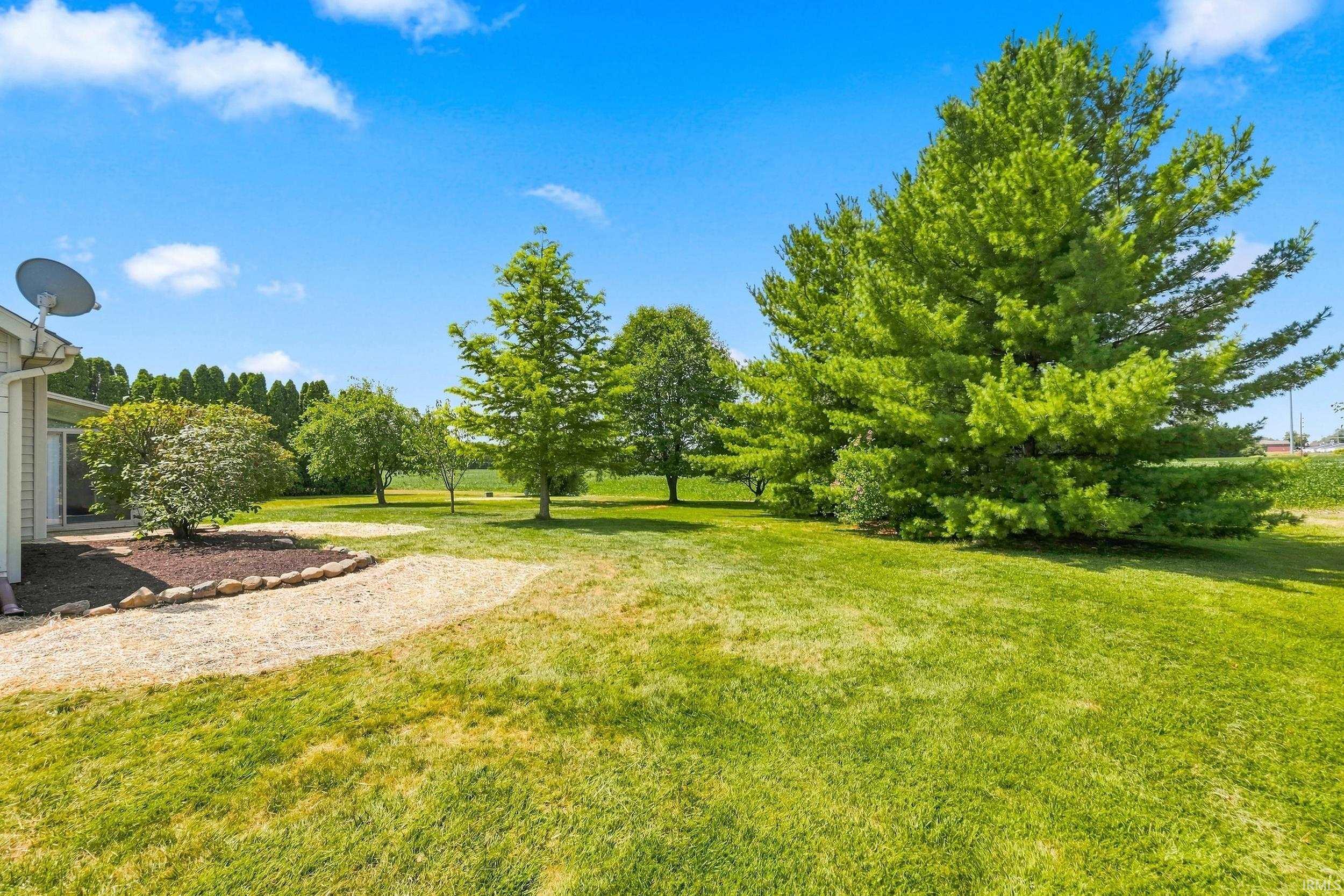 Expansive green lawn with mature trees and a gravel pathway leading to a landscaped bed