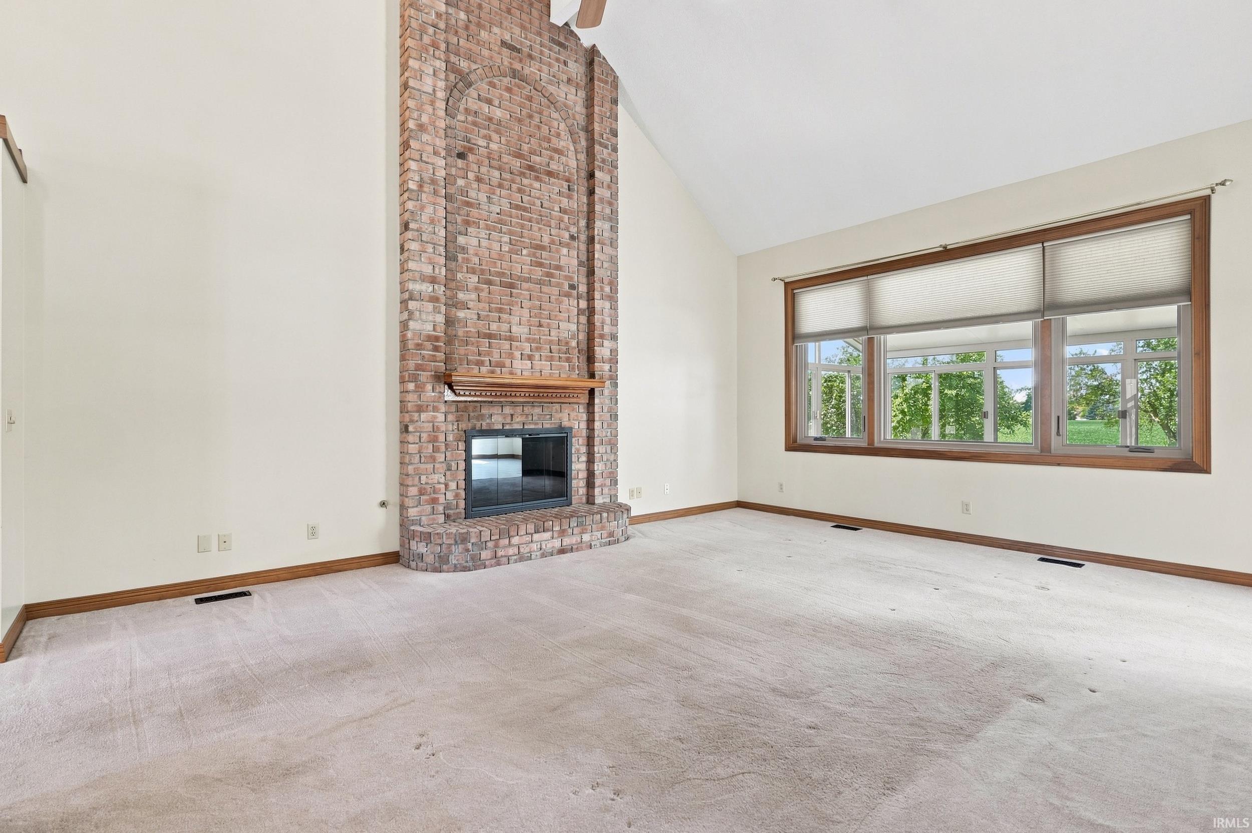 Vaulted ceiling room featuring a full-height brick fireplace with a wood mantle