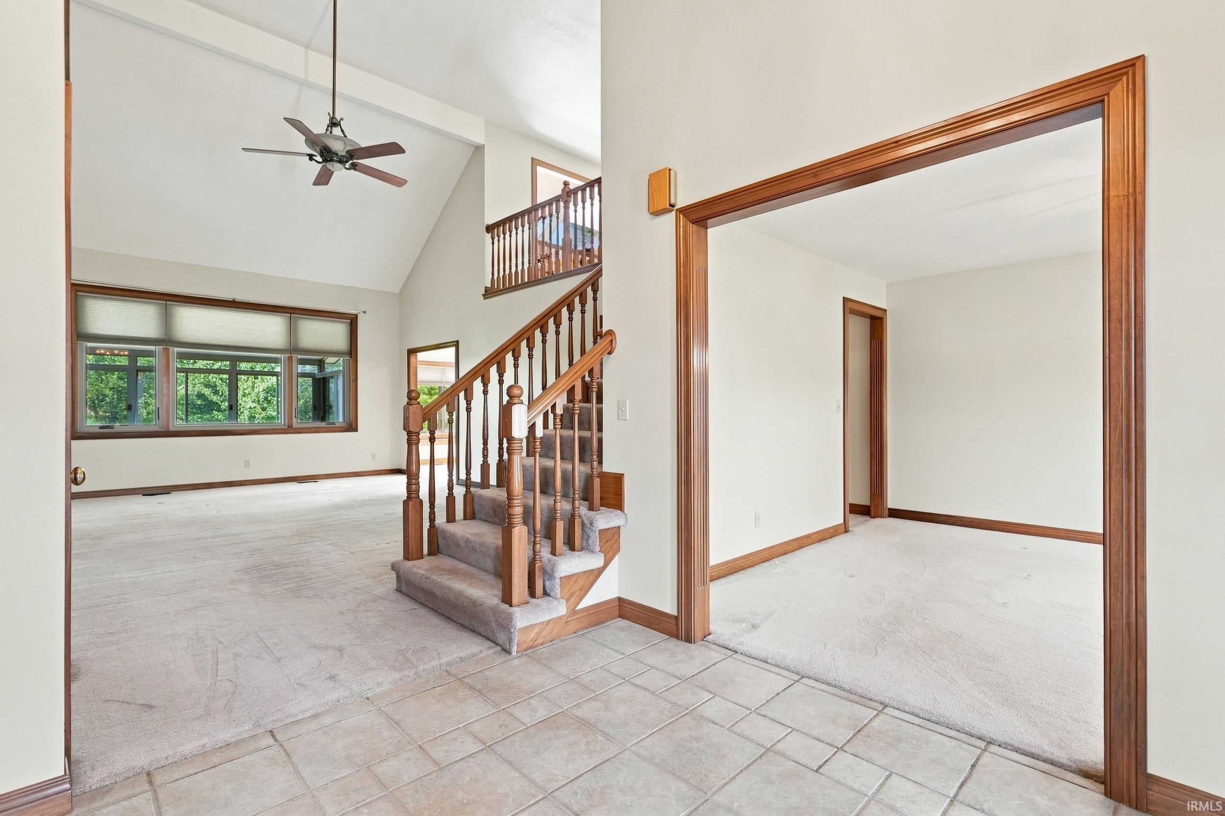 Foyer with tile flooring leading to a carpeted living area and a wooden staircase
