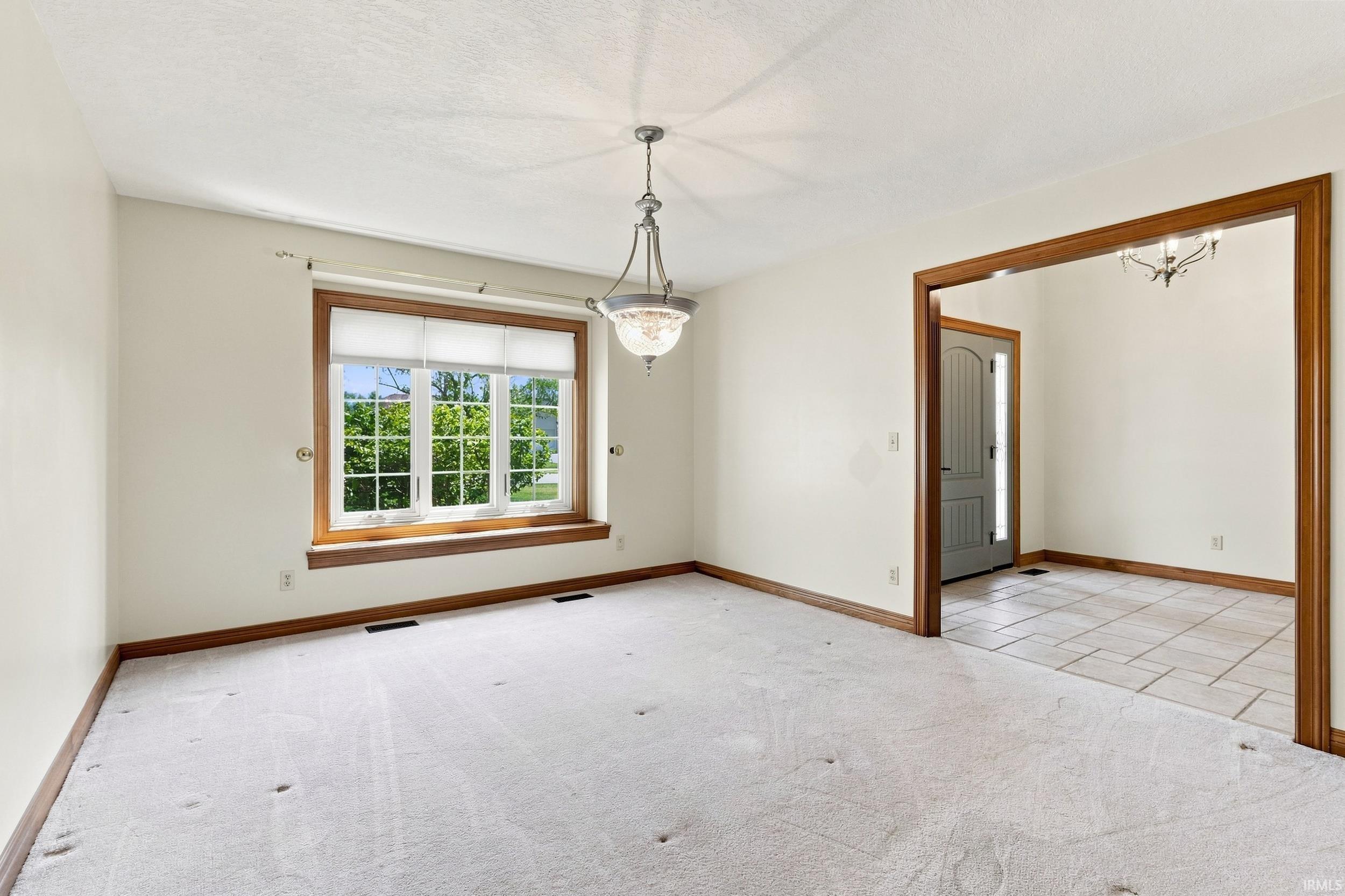 Inviting interior space featuring a large bay window with wood trim, neutral carpeting, and a polished nickel chandelier