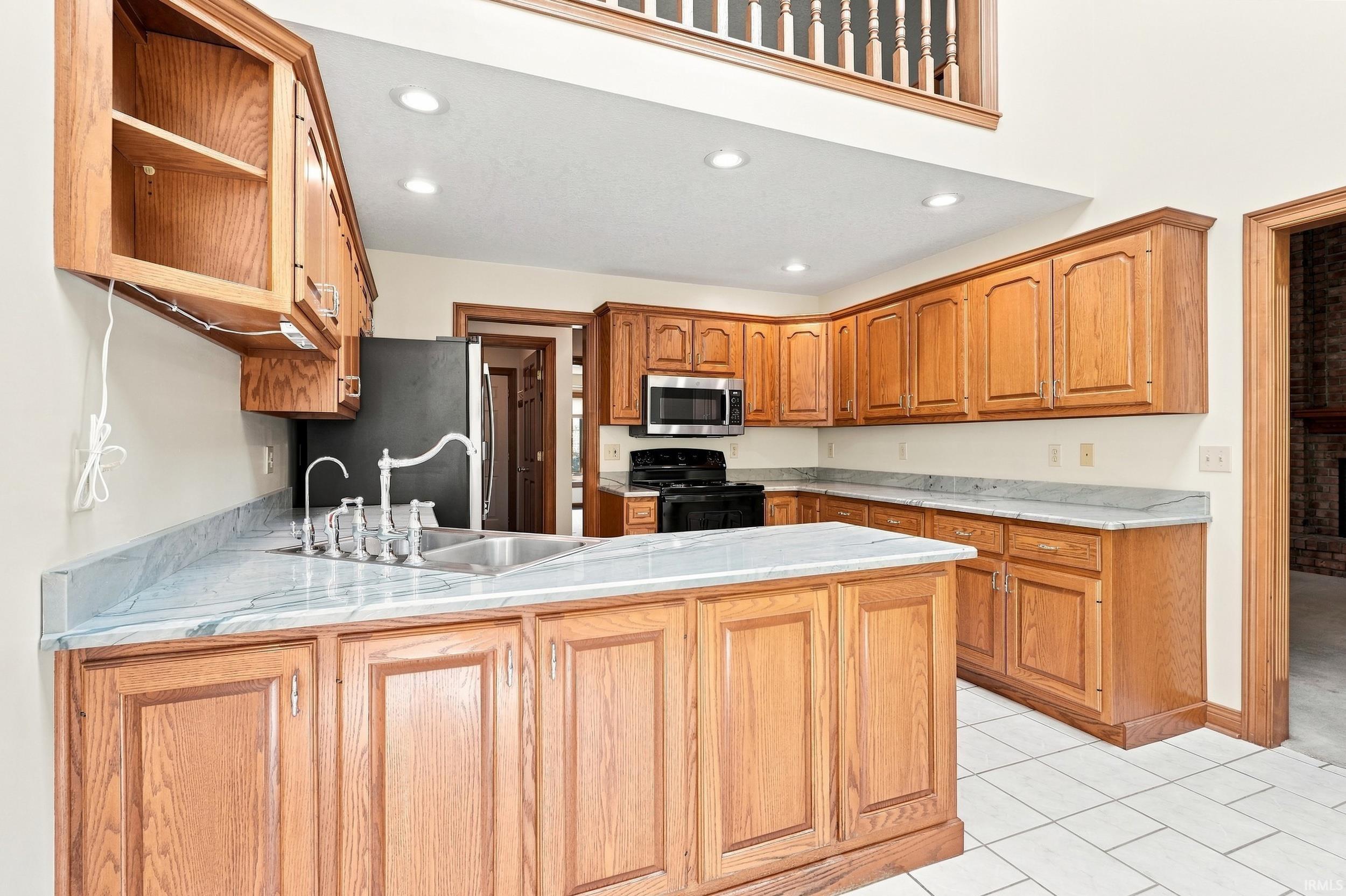 Kitchen featuring wood cabinetry, light-toned countertops, a stainless steel double basin sink with a gooseneck faucet, a built-in microwave, and recessed ceiling lighting