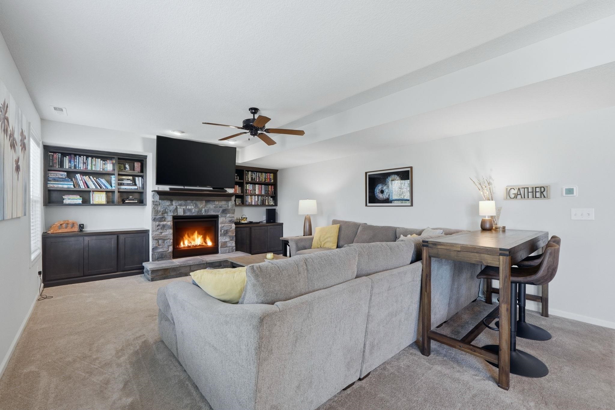 Carpeted living area featuring a stone fireplace and ceiling fan