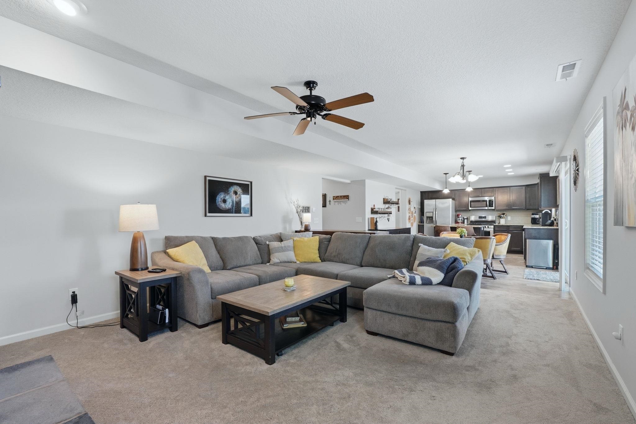 Living room with ceiling fan, suspended lighting, and light carpet