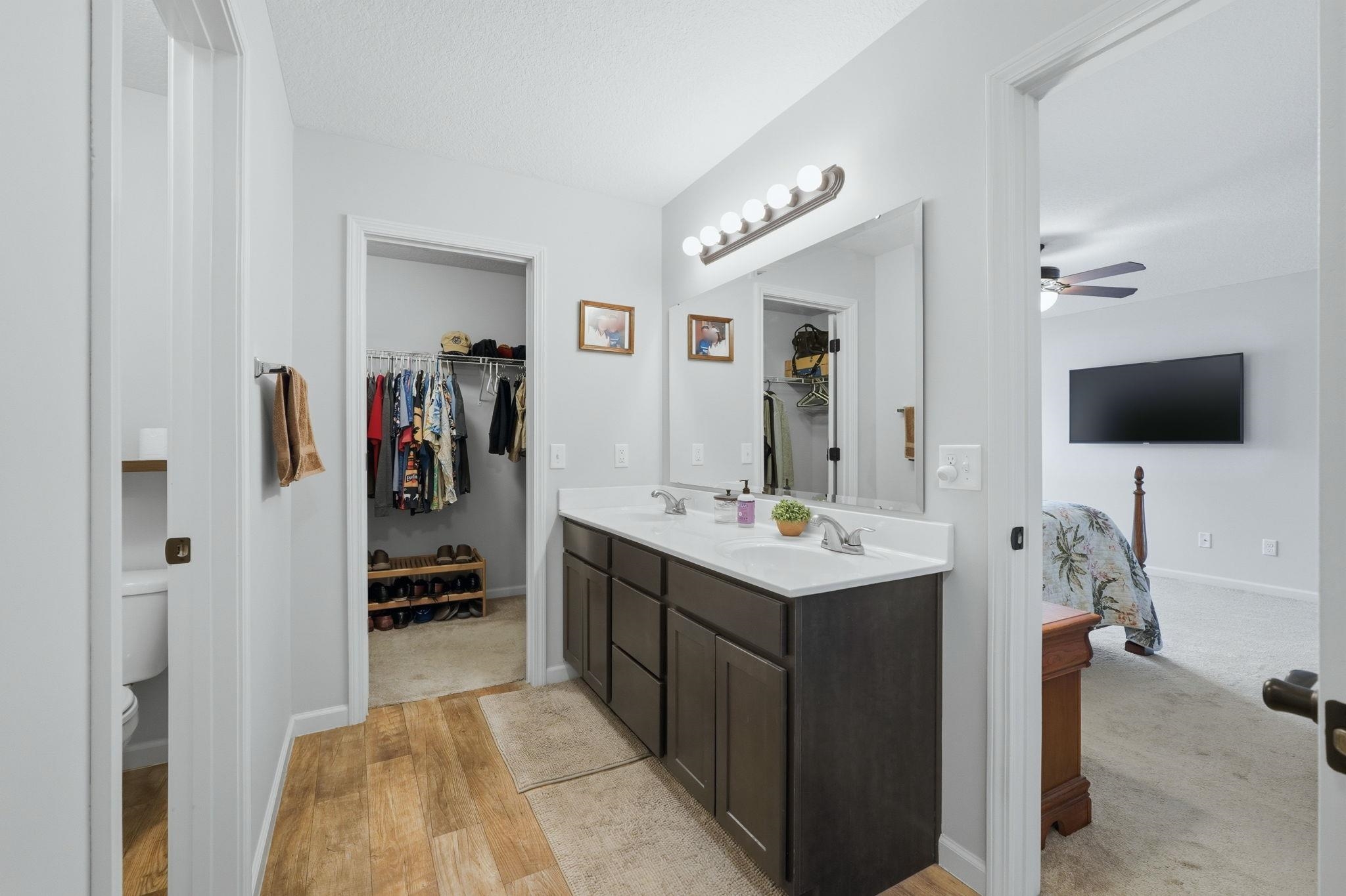Dual vanity with white countertop, chrome fixtures, wood-finish flooring, and a walk-in closet with built-in shelving