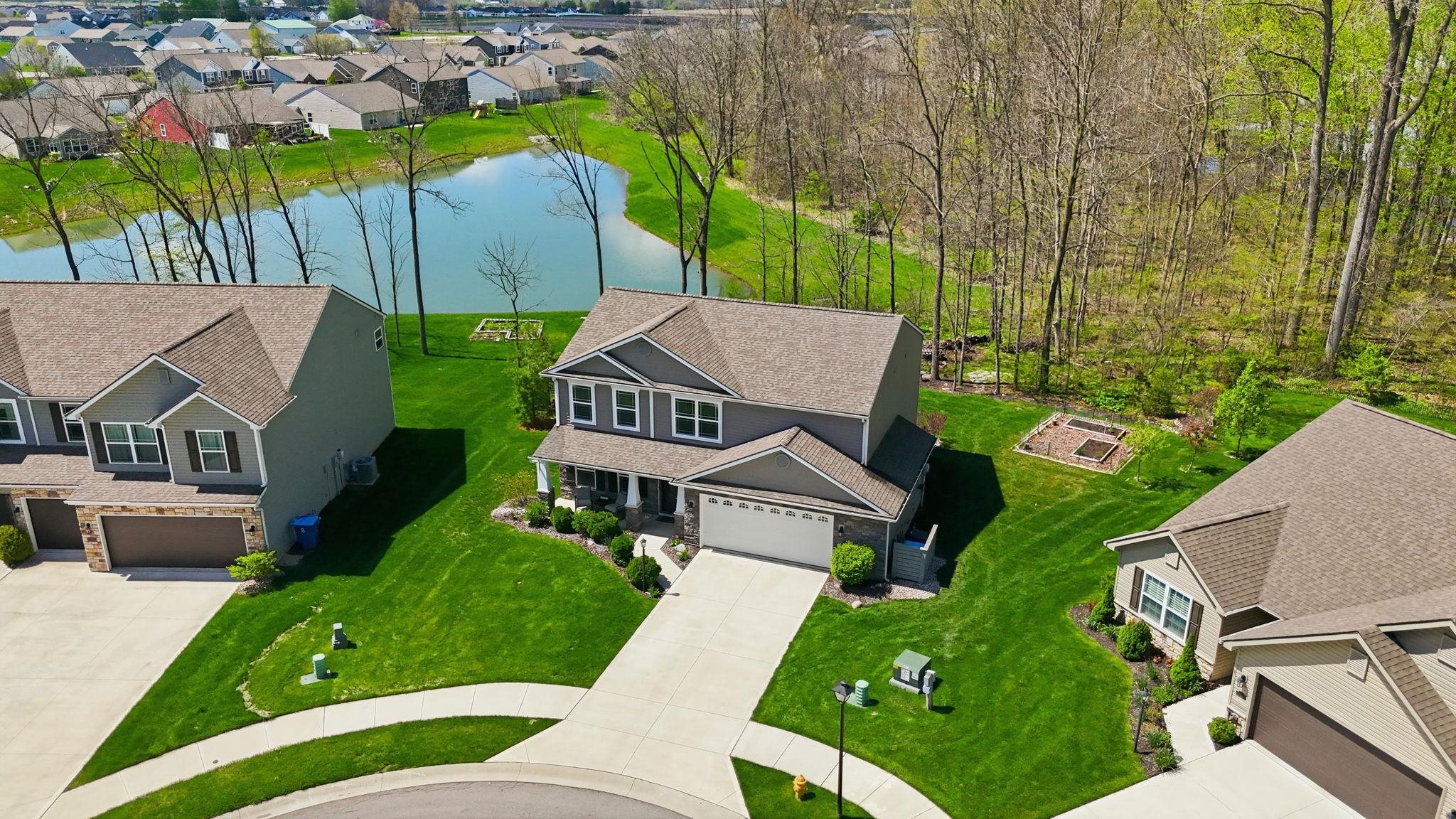 Contemporary two-story residence featuring a two-car garage, covered front porch, and a rear yard bordering a pond and natural woodlands