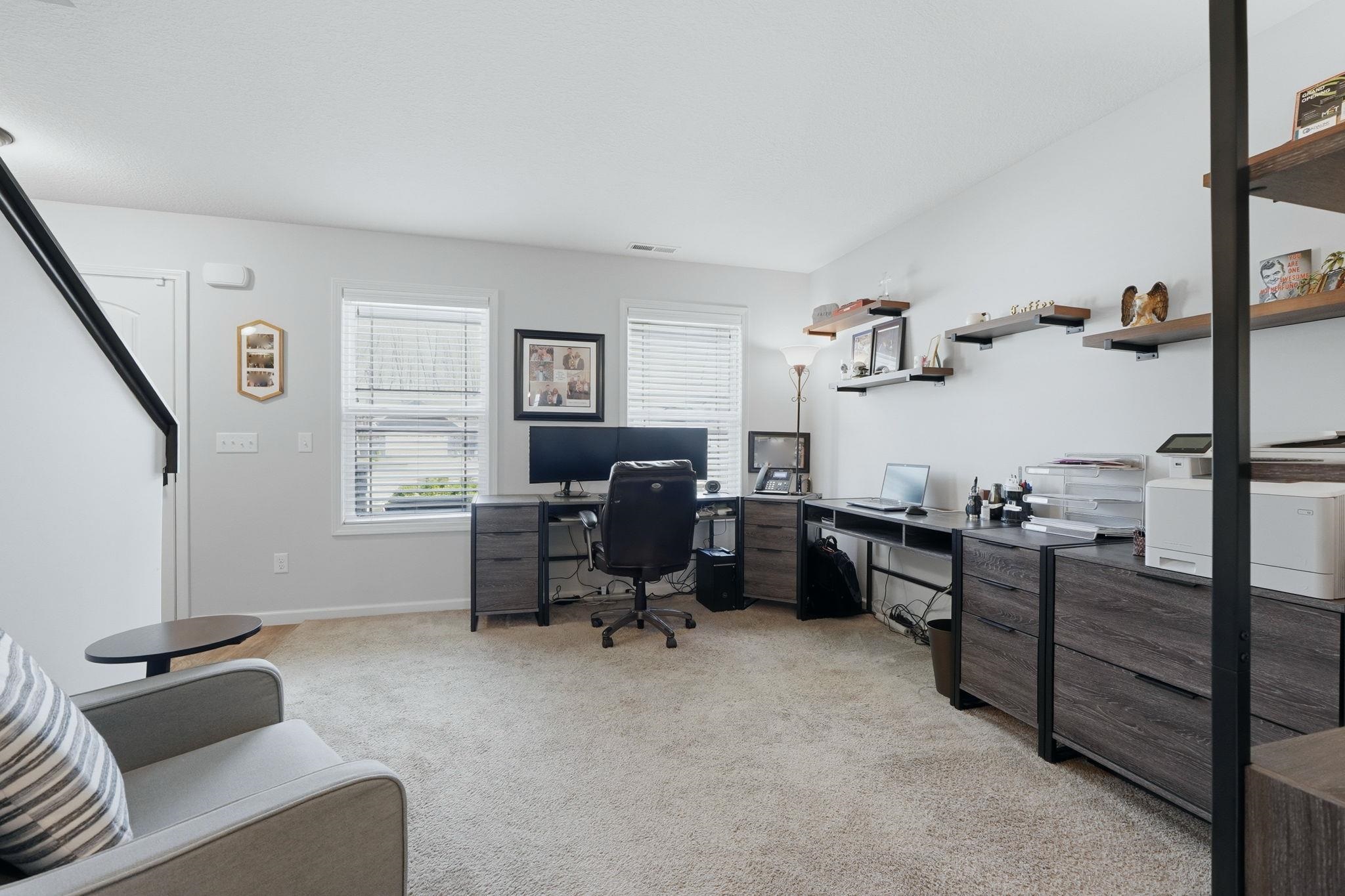 Carpeted room with multiple windows, wall-mounted shelving, and a black staircase railing