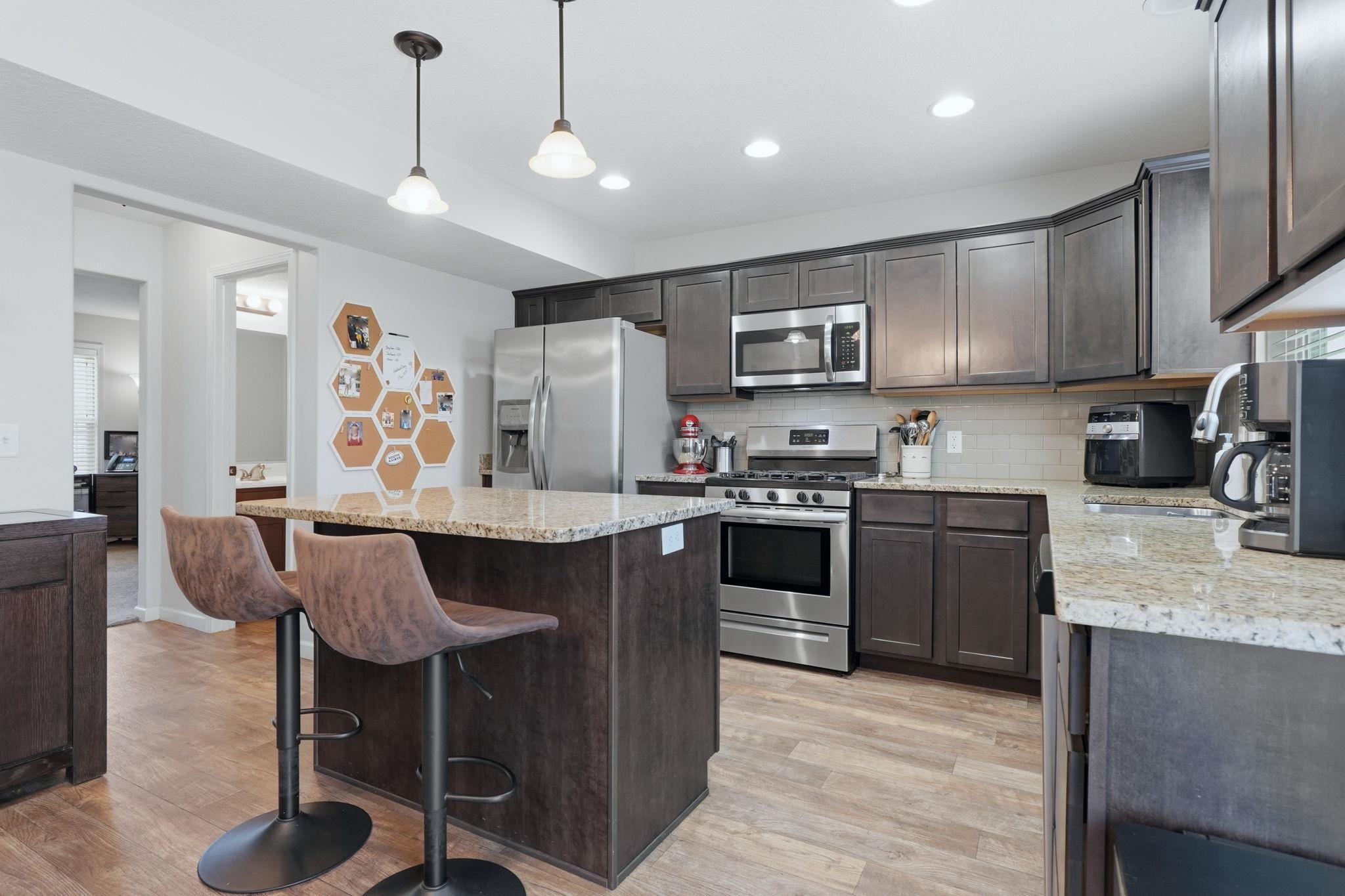 Kitchen featuring dark wood-finish cabinetry, stainless steel appliances, granite countertops, and wood-finish flooring