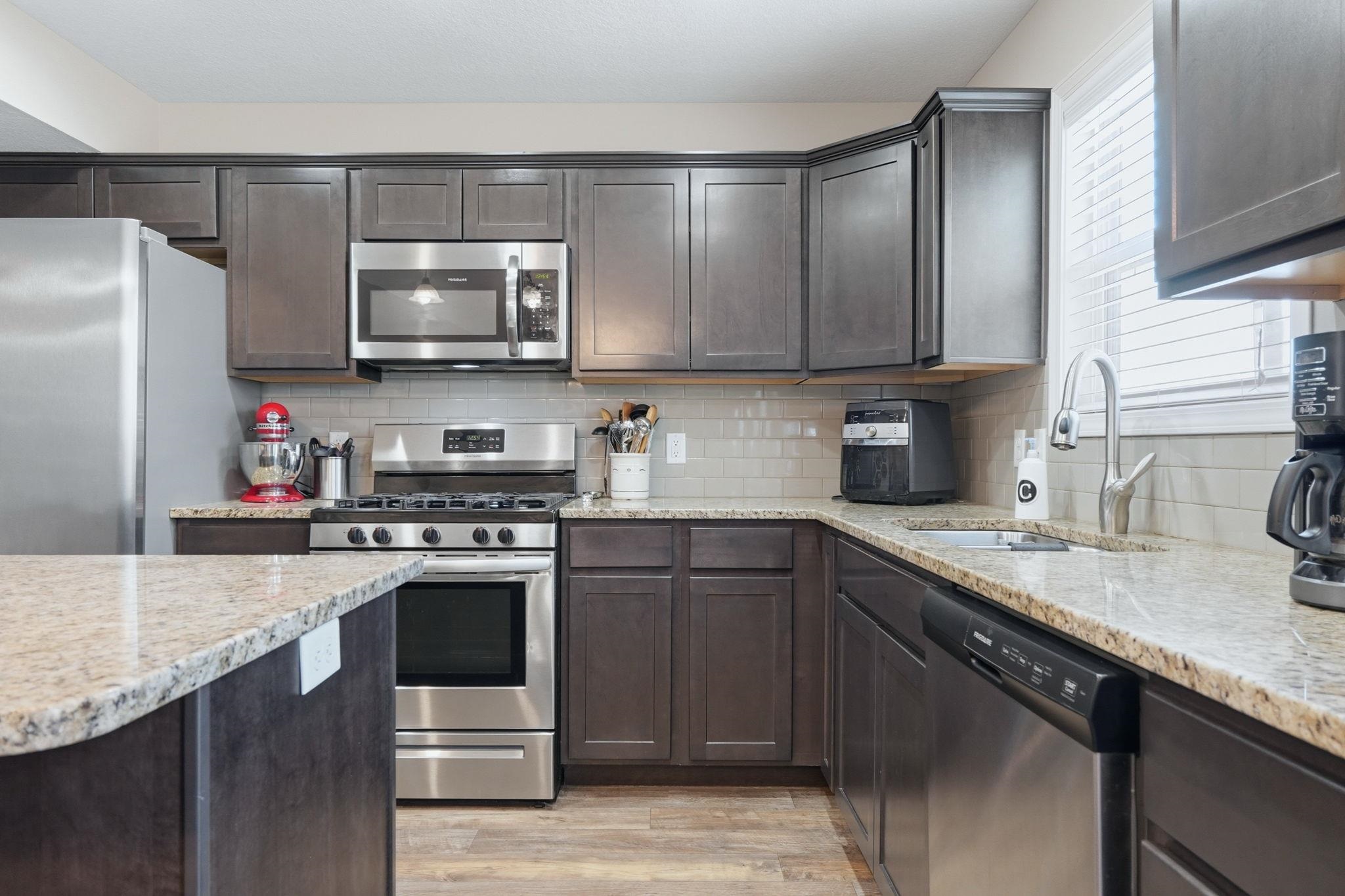 Kitchen with stainless steel appliances, dark wood finish cabinetry, and healthy amount of natural light