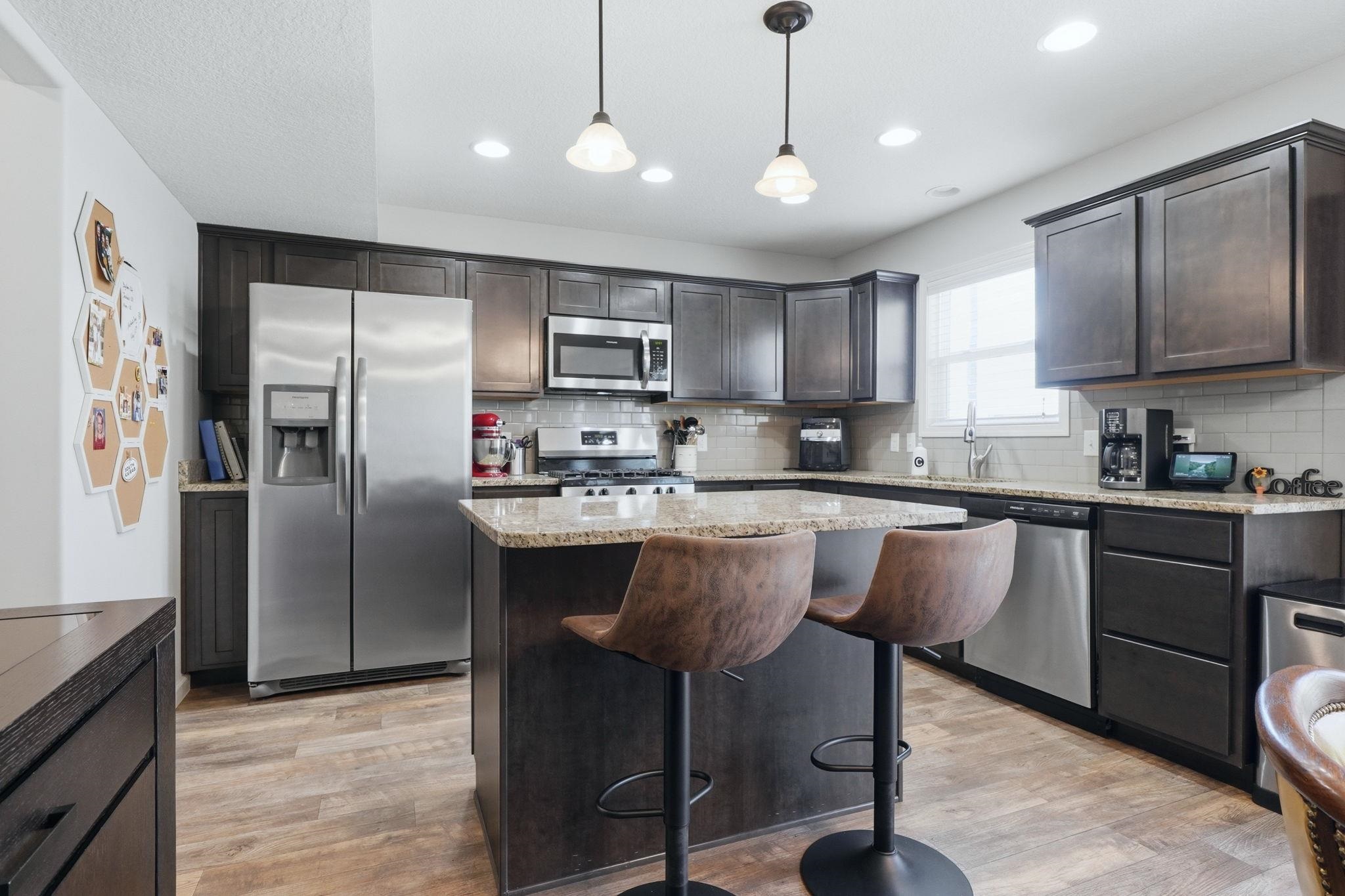 Kitchen with stainless steel appliances, a kitchen island, dark wood finish cabinets, pendant lighting, and light wood-style floors
