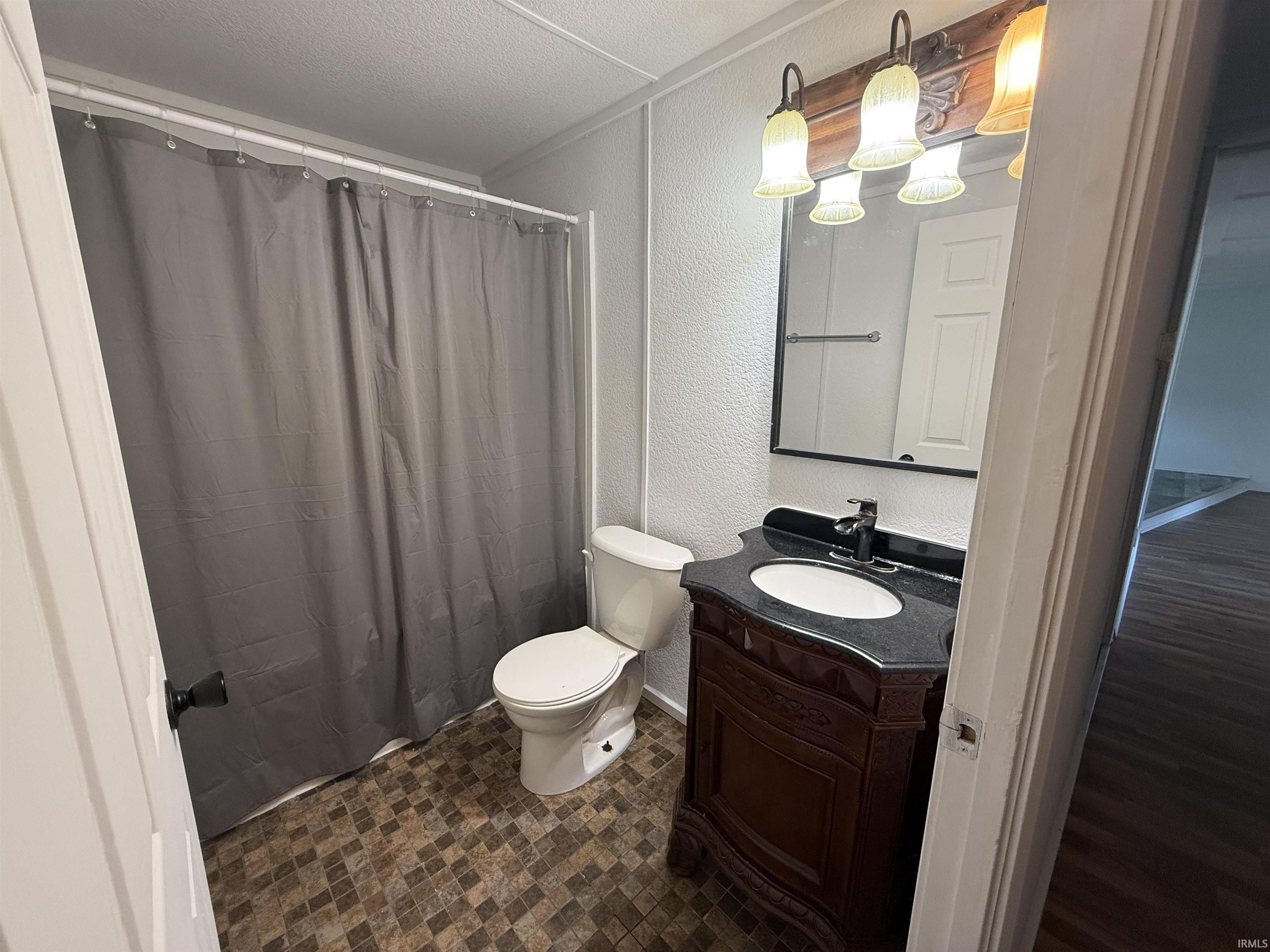 Bathroom featuring a dark wood vanity with an integral white sink, black countertop, and a wall-mounted mirror with a four-light fixture