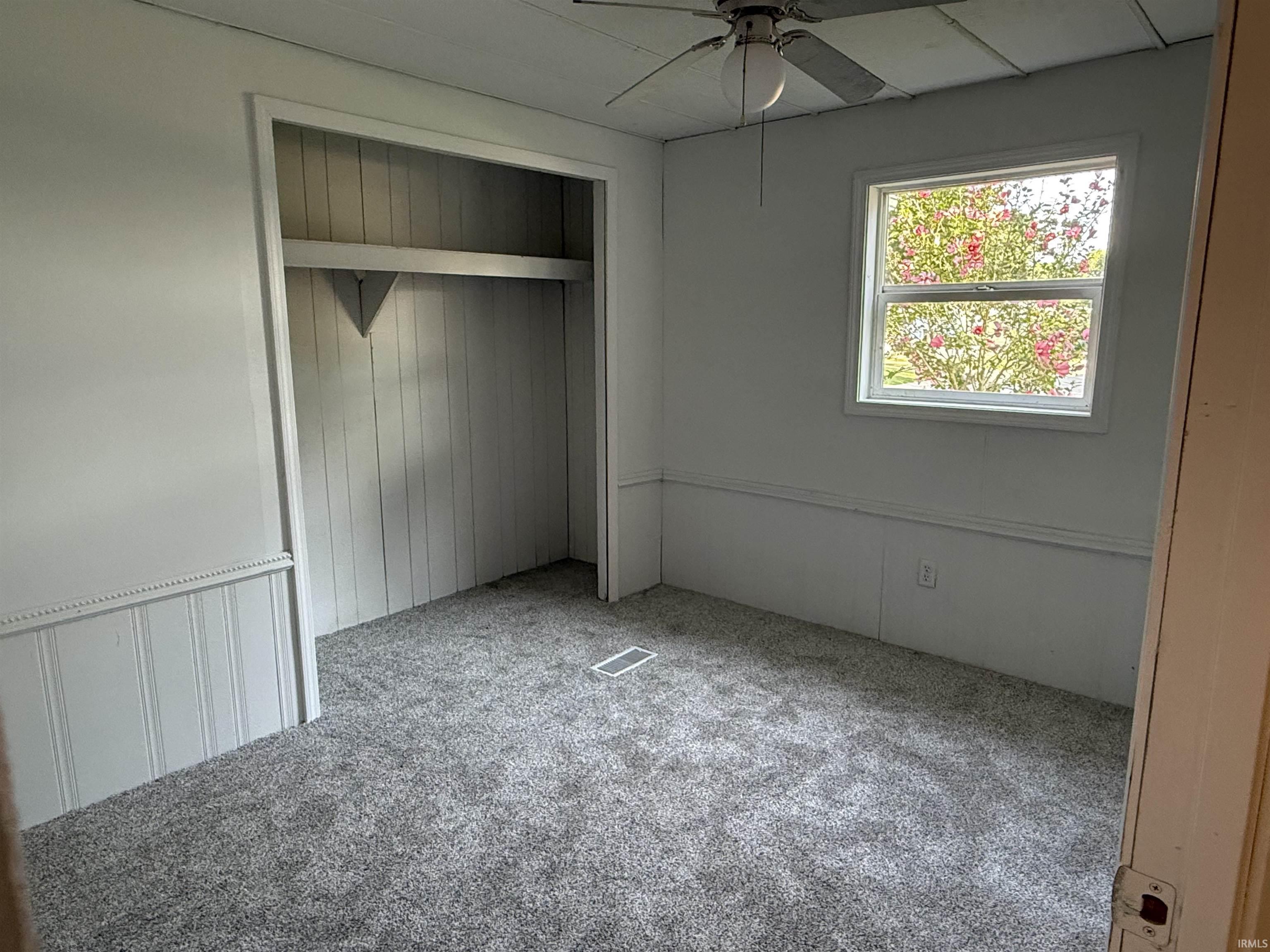 Room featuring a built-in closet with shelving, a single window, a ceiling fan with integrated lighting, and wall paneling
