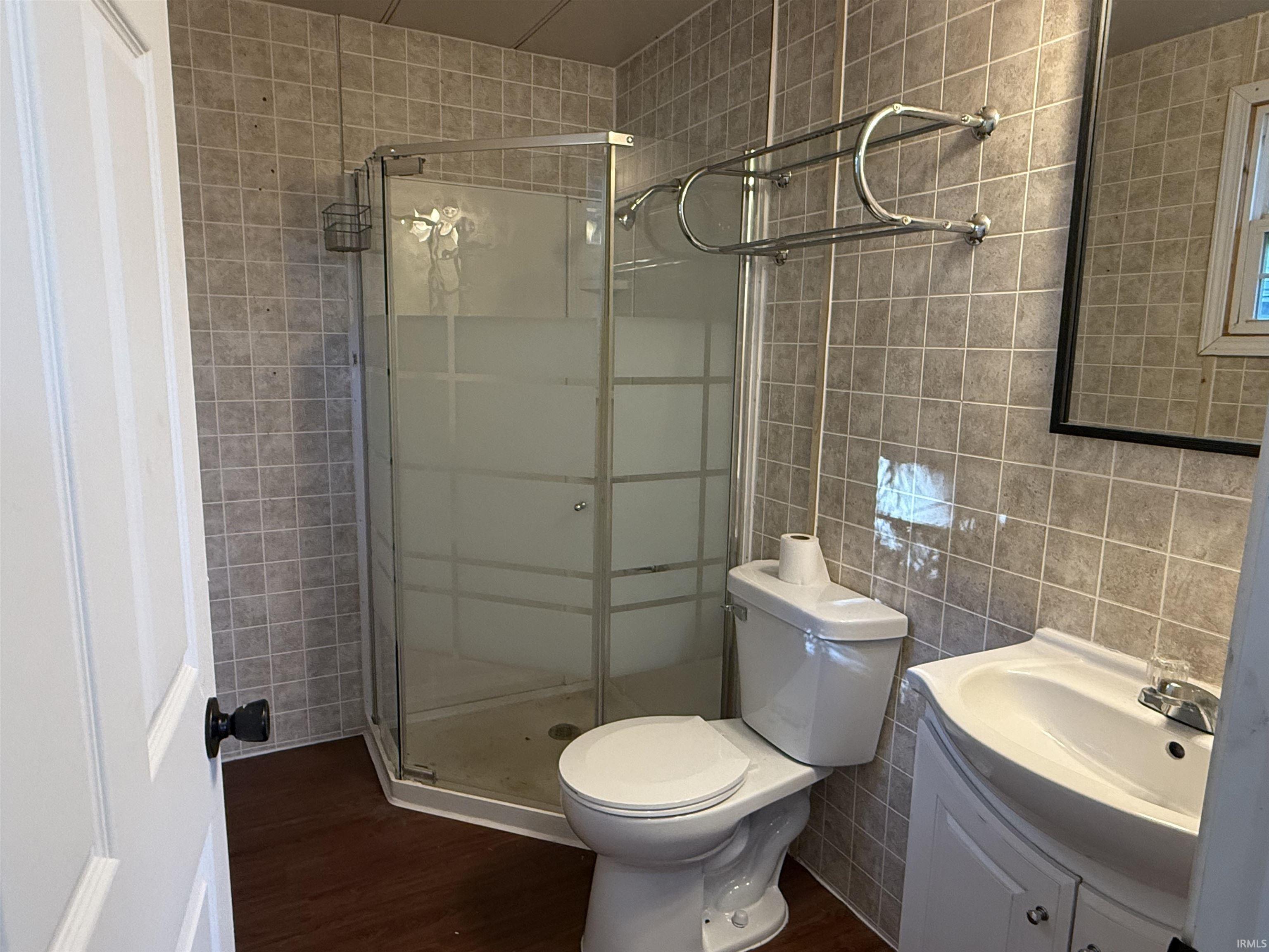 Corner shower enclosure with frosted glass panels, surrounded by square-tiled walls