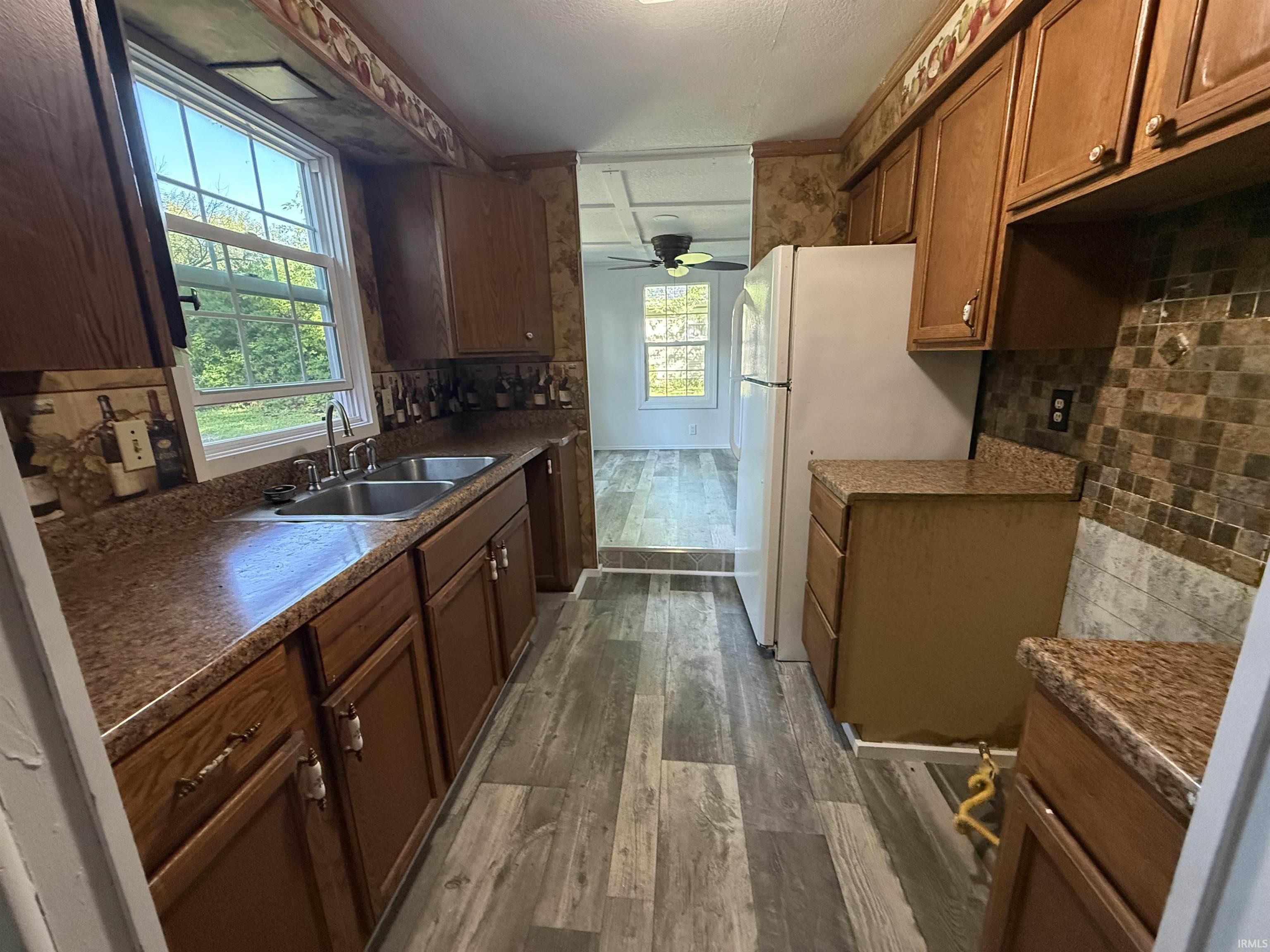 Galley kitchen featuring wood-finish cabinetry, granite-look countertops, and a double basin stainless steel sink