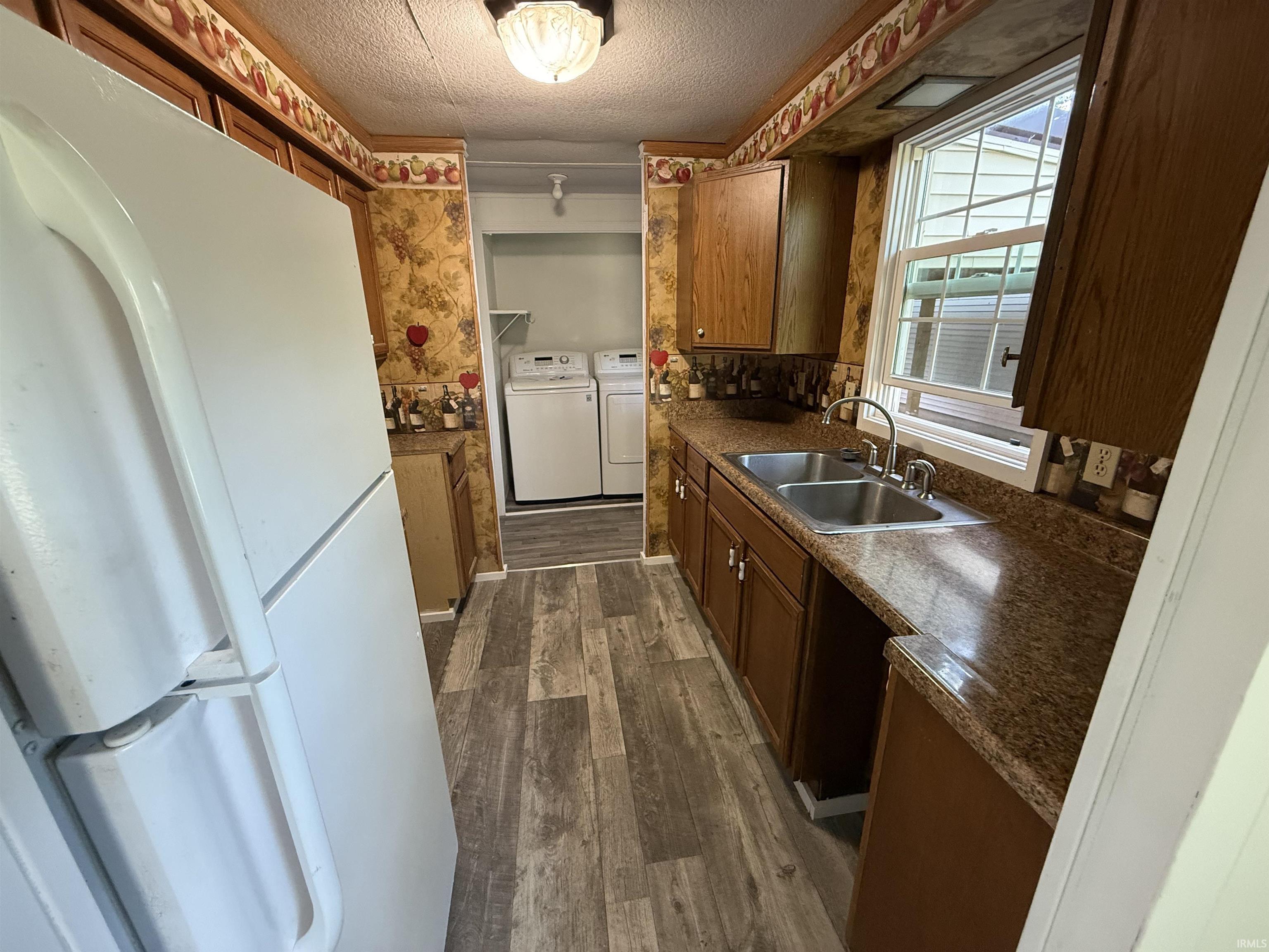 Galley-style kitchen featuring wood-finish flooring, wood cabinetry, granite-look countertops, and a double basin stainless steel sink
