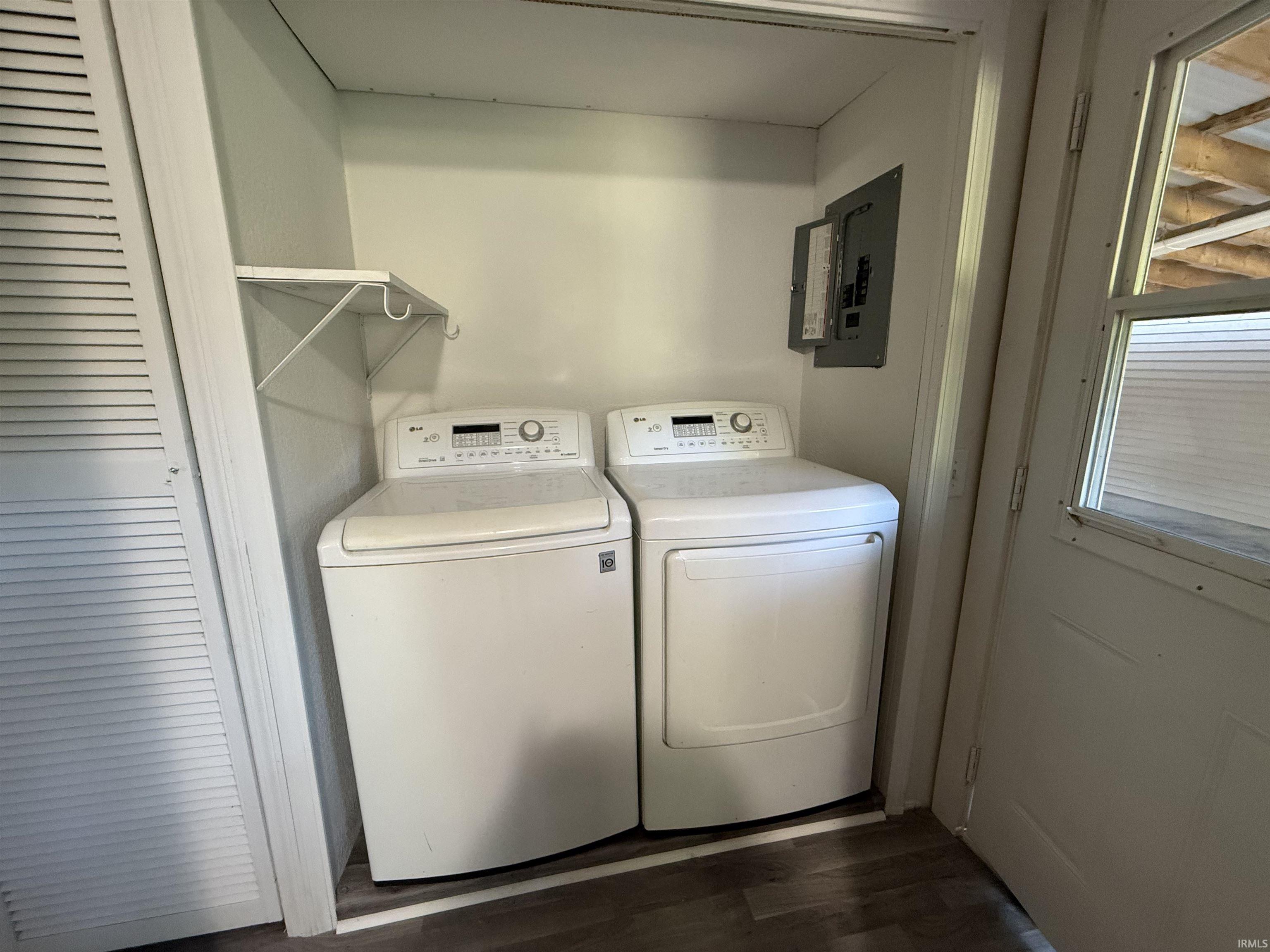 Dedicated laundry area featuring wood-finish flooring, louvered bi-fold doors, and an overhead storage shelf