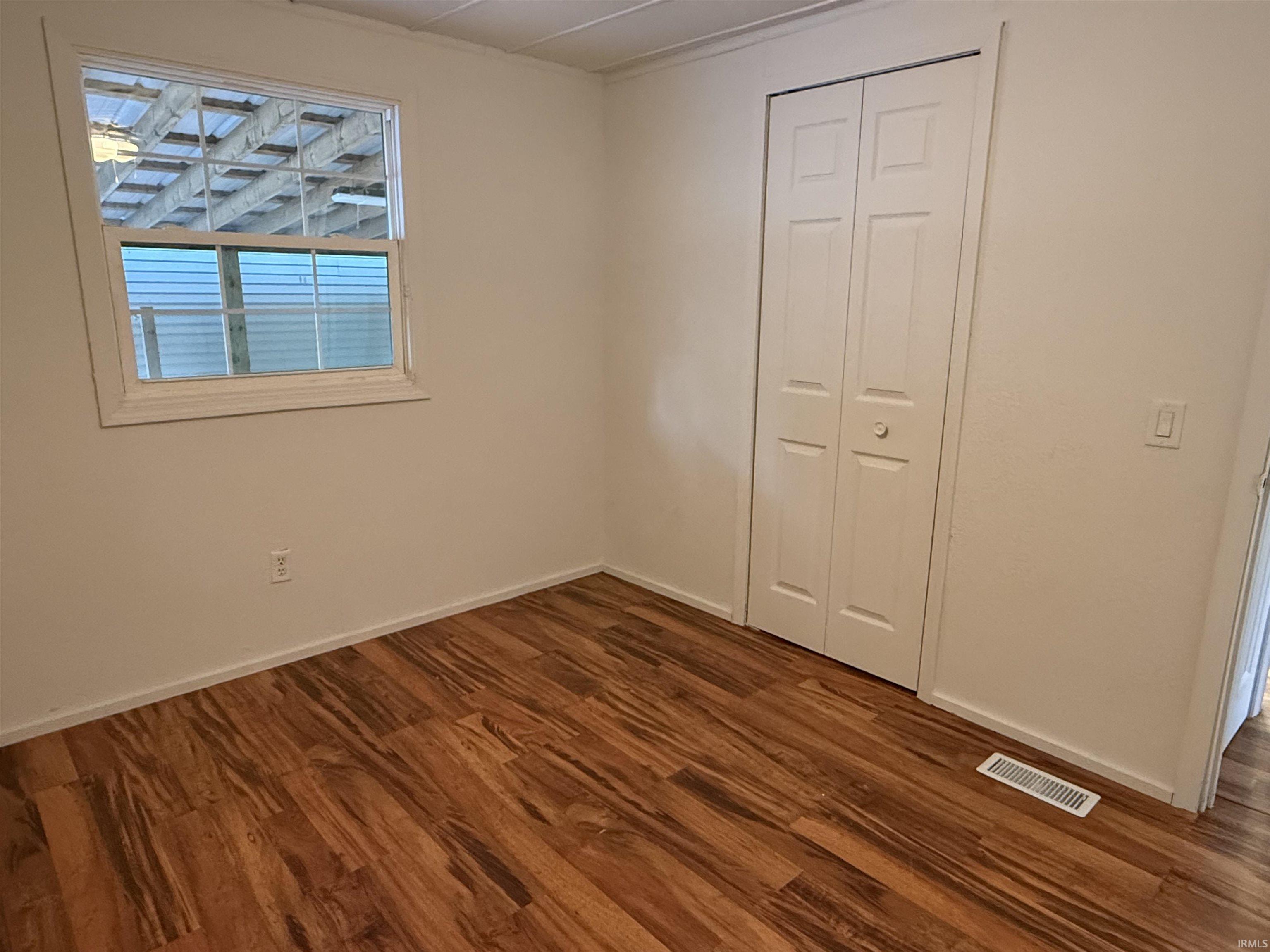 Room featuring wood-finish flooring, white walls, and a bi-fold closet