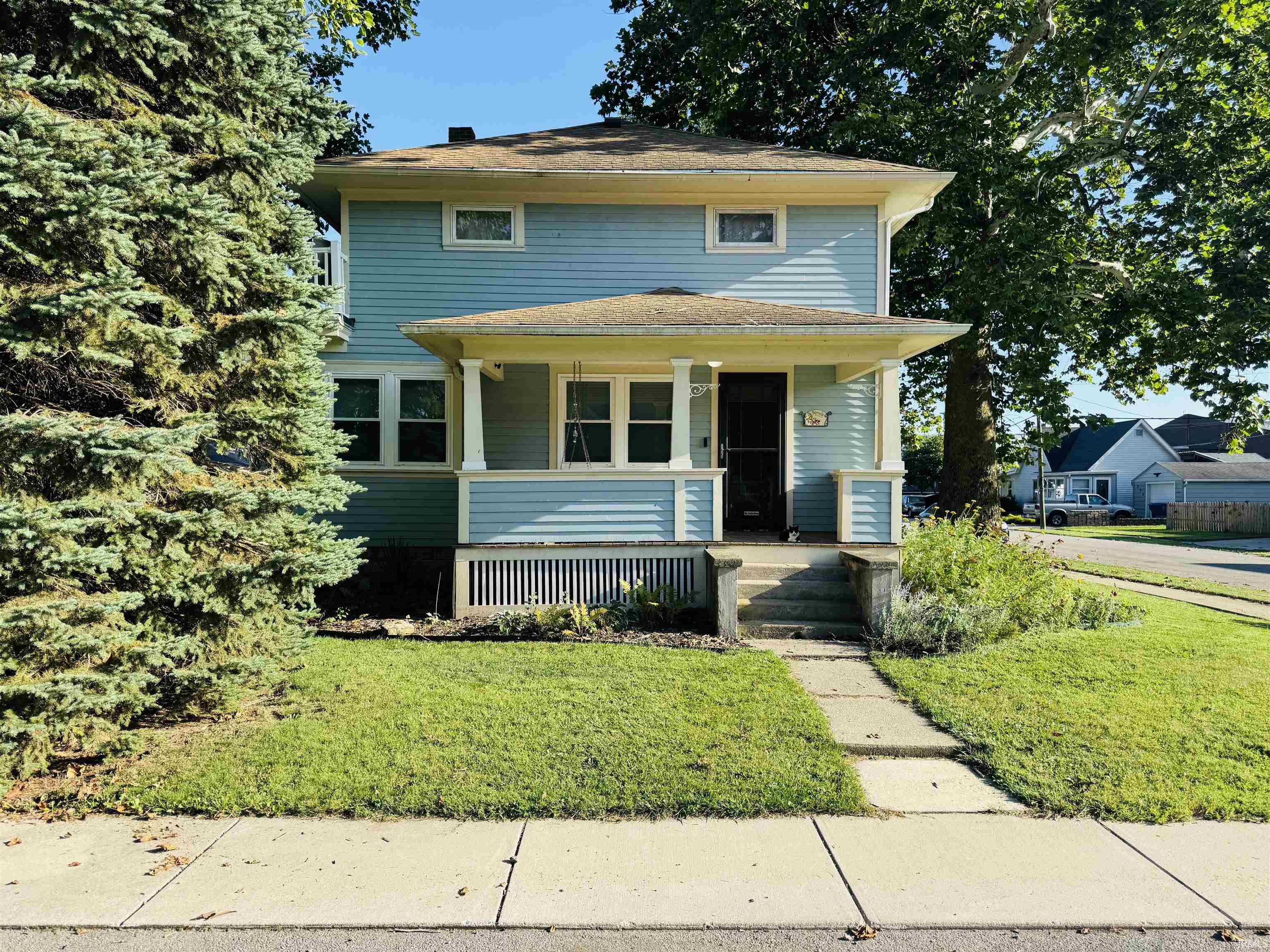 Light blue siding exterior featuring a covered porch with white columns, a concrete walkway, and a manicured lawn