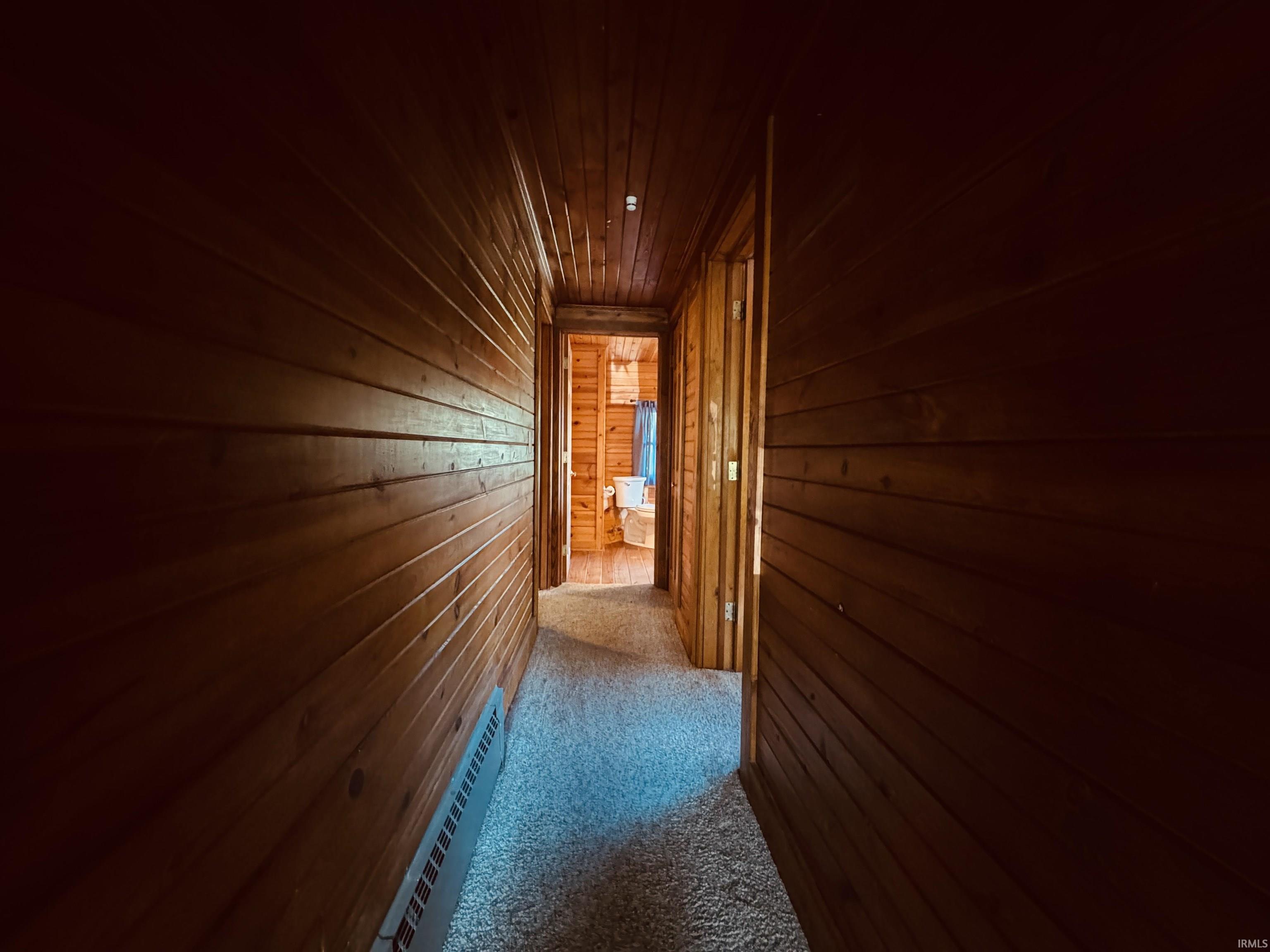 Hallway featuring wood-paneled walls and ceiling, wall-to-wall carpeting, and baseboard heating
