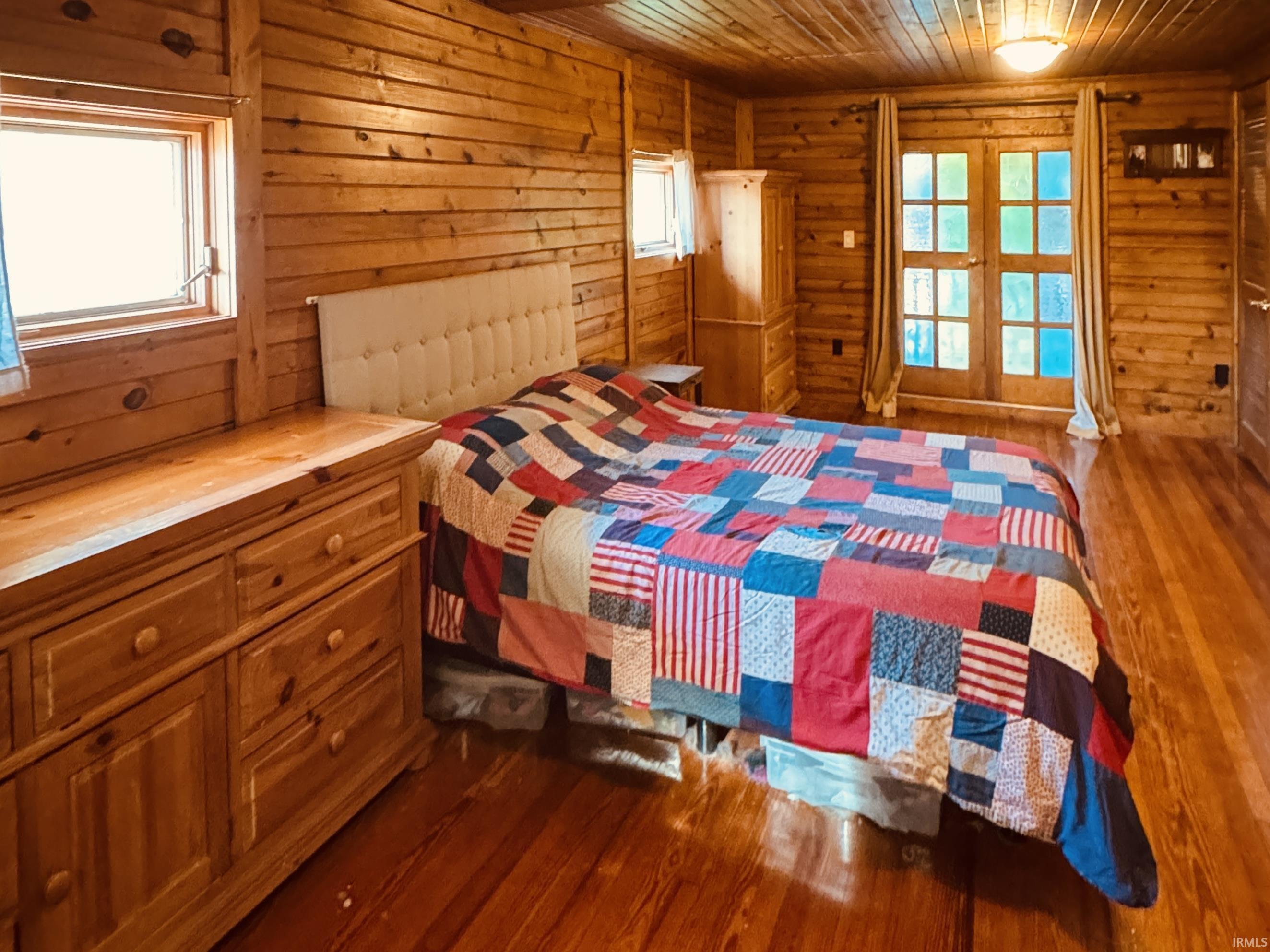 Warm wood-finish bedroom featuring knotty pine walls and ceiling, hardwood flooring throughout, and substantial built-in wooden cabinetry with multiple drawers