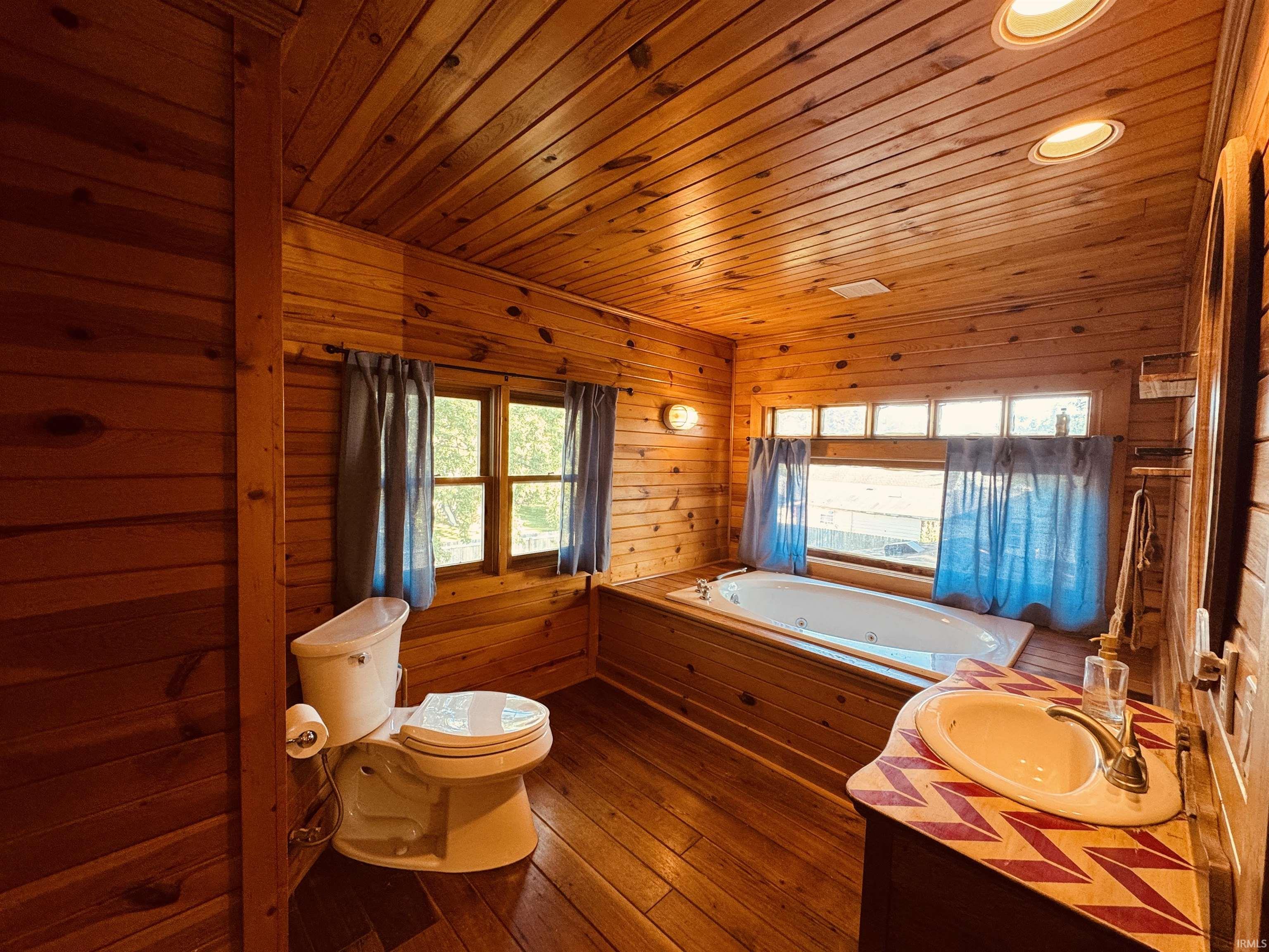 Wood-paneled bathroom featuring a built-in jetted tub, a vanity with an integrated sink, and recessed ceiling lighting