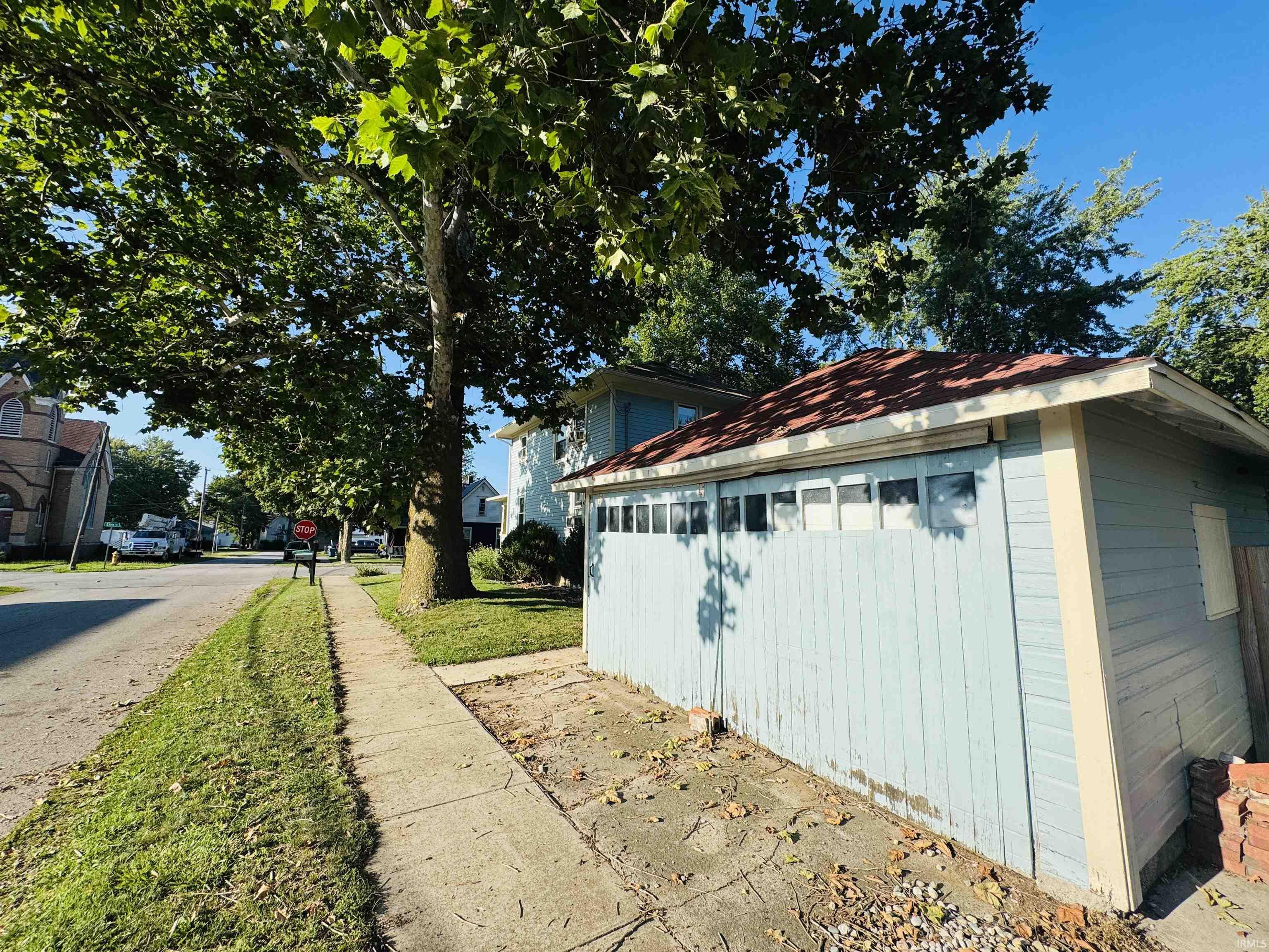 Detached garage structure featuring light blue vertical siding and a red shingle roof