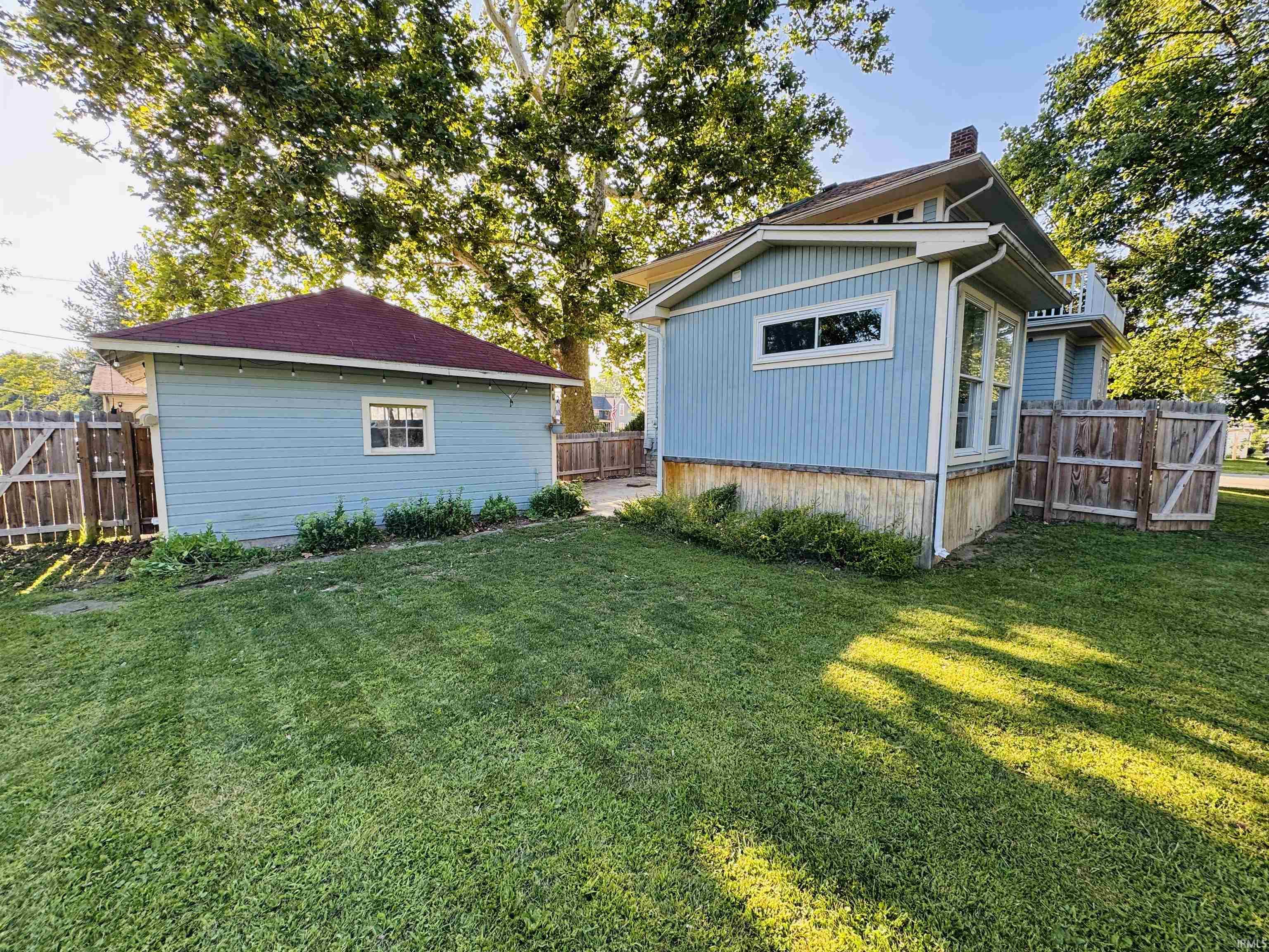 Expansive lawn area featuring a detached garage with a red shingle roof and a light blue exterior, alongside the primary residence with matching light blue siding