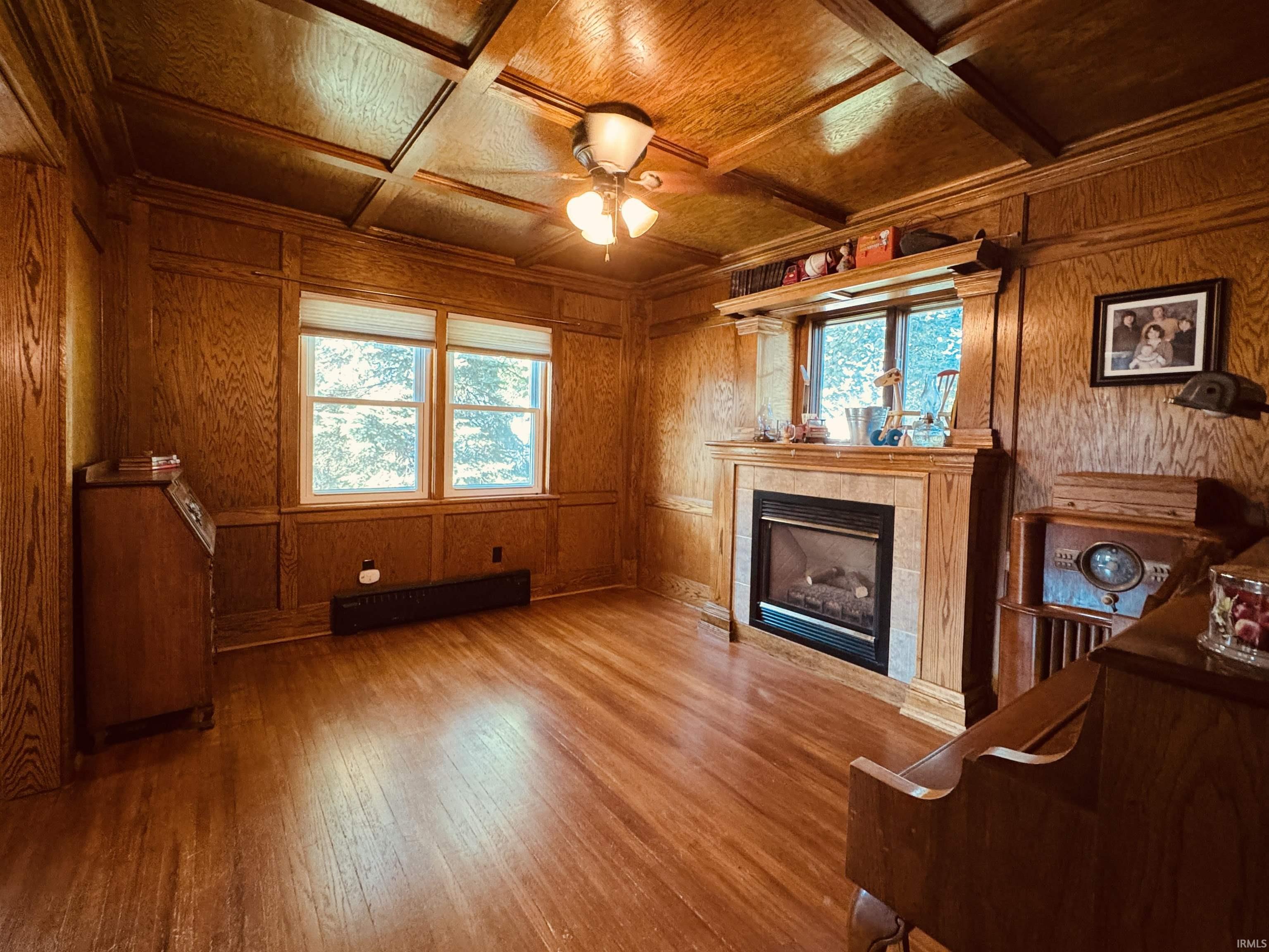 Wood-paneled room featuring a coffered ceiling, wood-finish flooring, a built-in fireplace with a stone surround, and dual windows