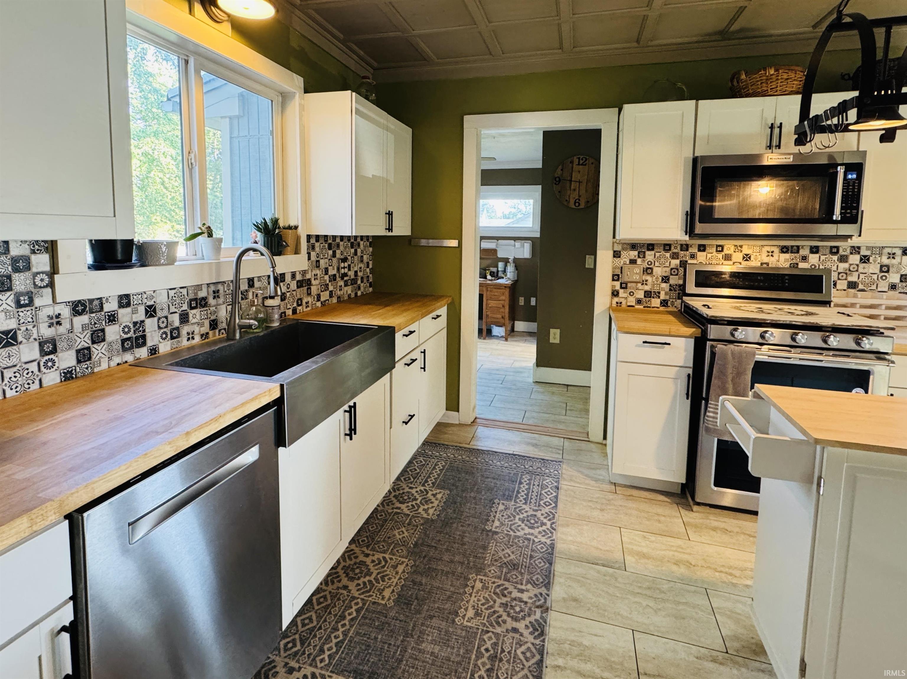 Kitchen featuring white cabinetry, wood-finish countertops, stainless steel appliances, and a farmhouse-style sink