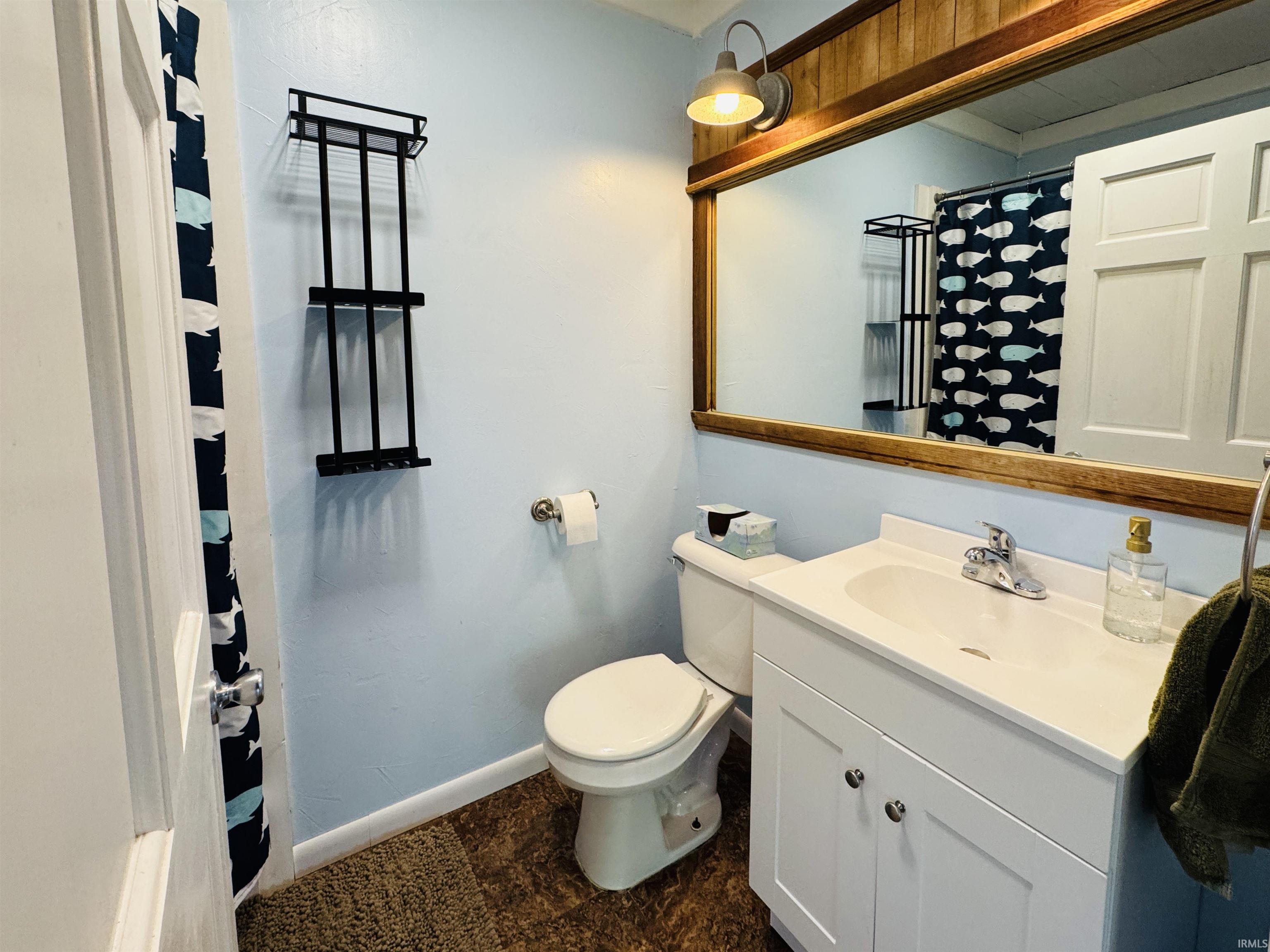 Contemporary bathroom featuring a single white vanity with a chrome faucet, a large wood-framed mirror, and wood-finish flooring
