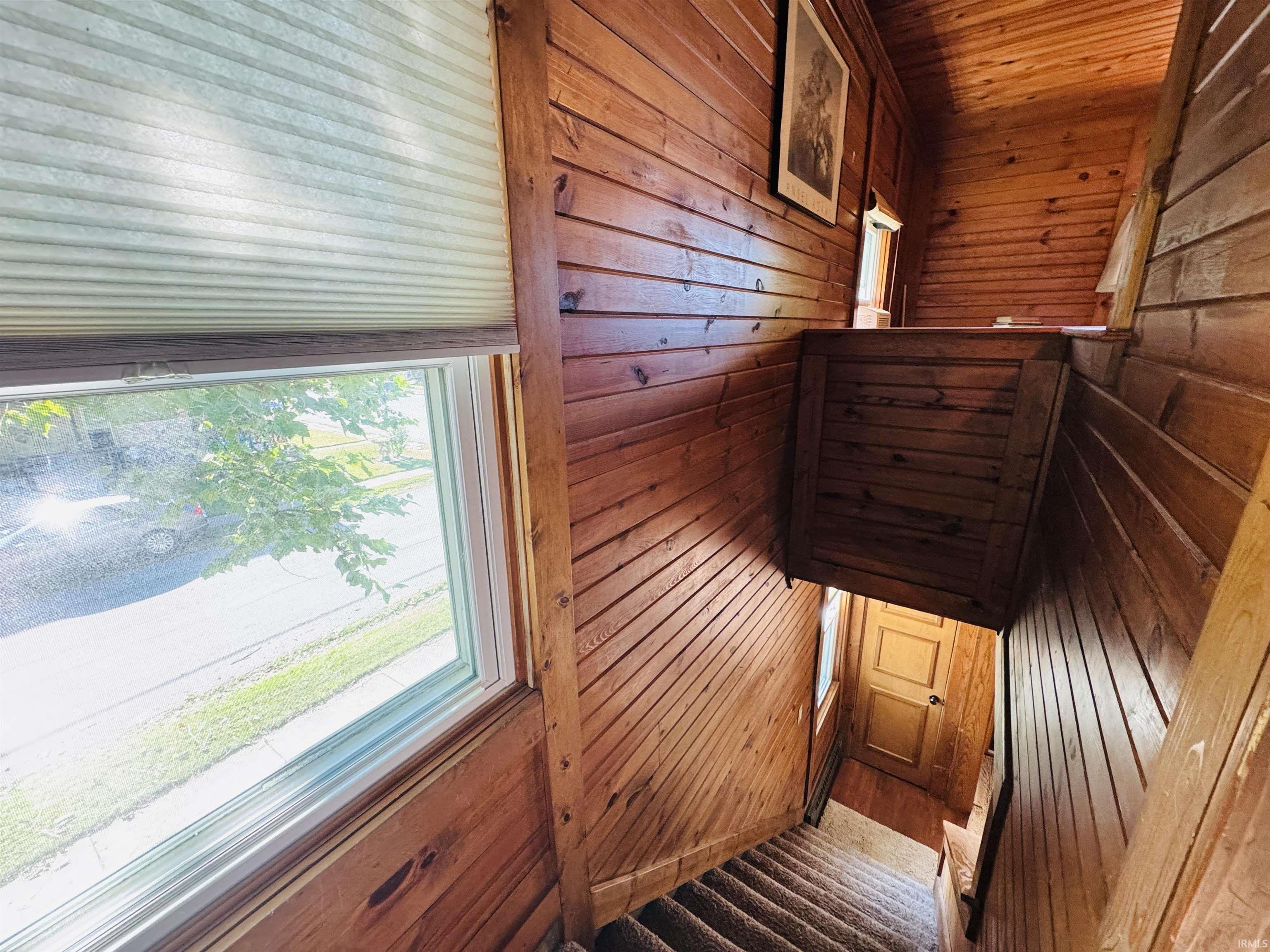Stairwell featuring paneled wood walls, carpeted treads, and a window with a cellular shade