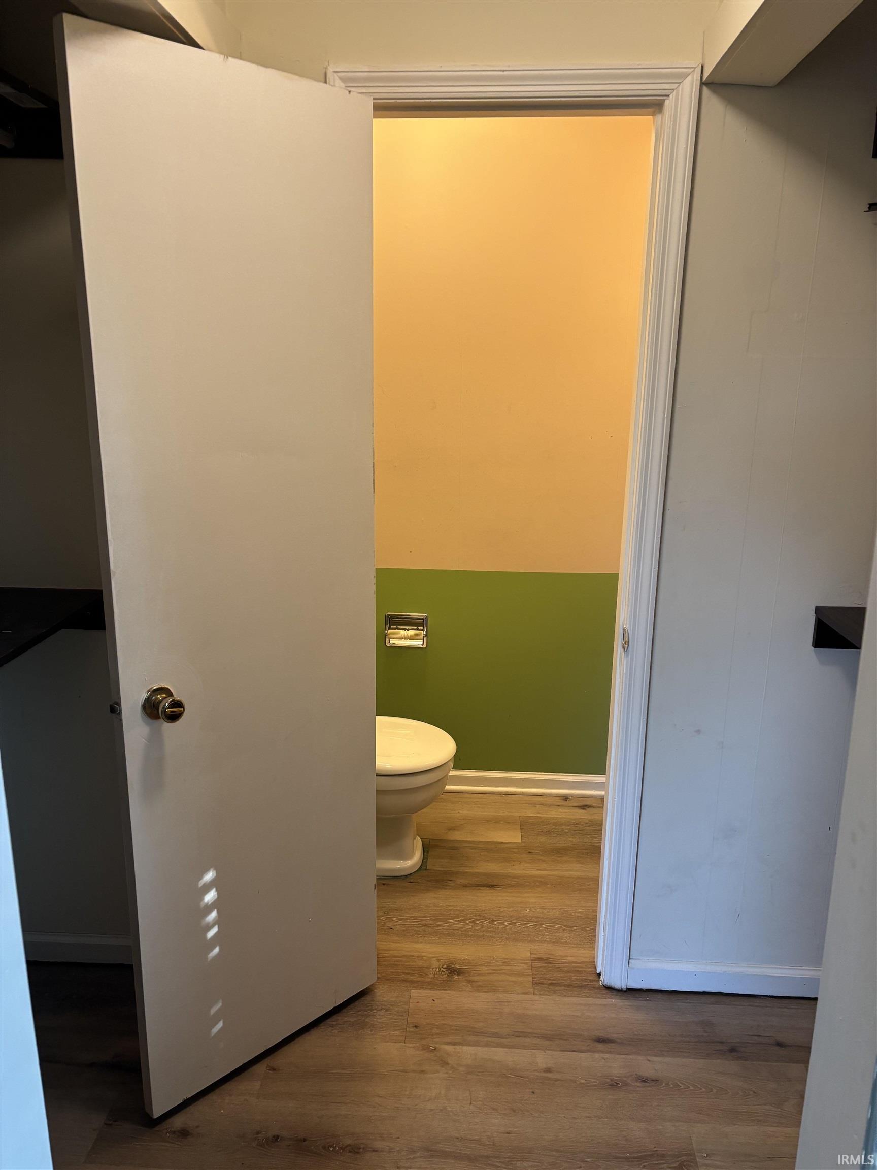 Bathroom with wood-finish flooring, a white toilet, two-tone wall paint, and white baseboards