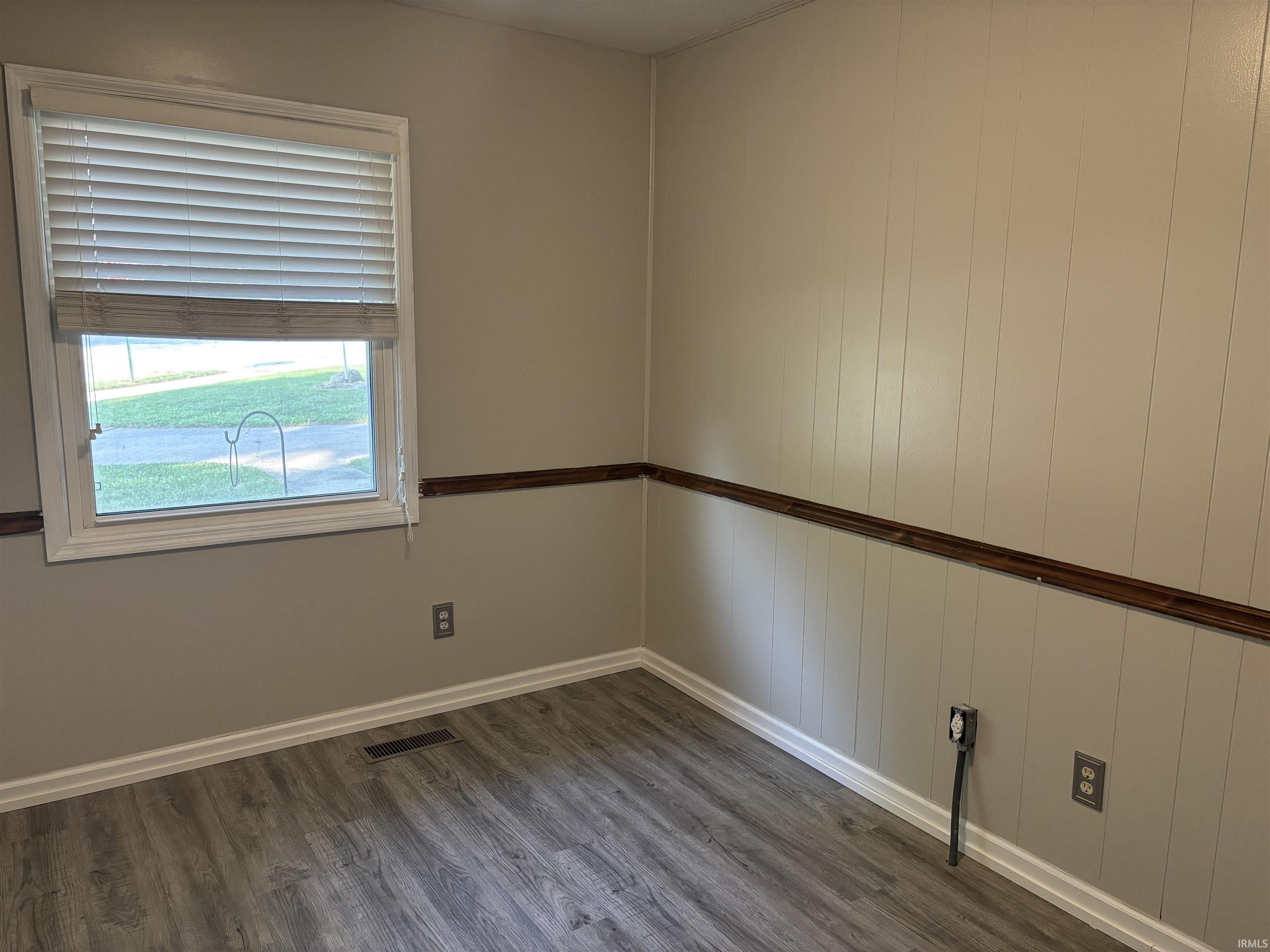 Window with blinds and a wood-finish sill, light gray wood-finish flooring, and light-colored wainscoting with a dark wood trim band