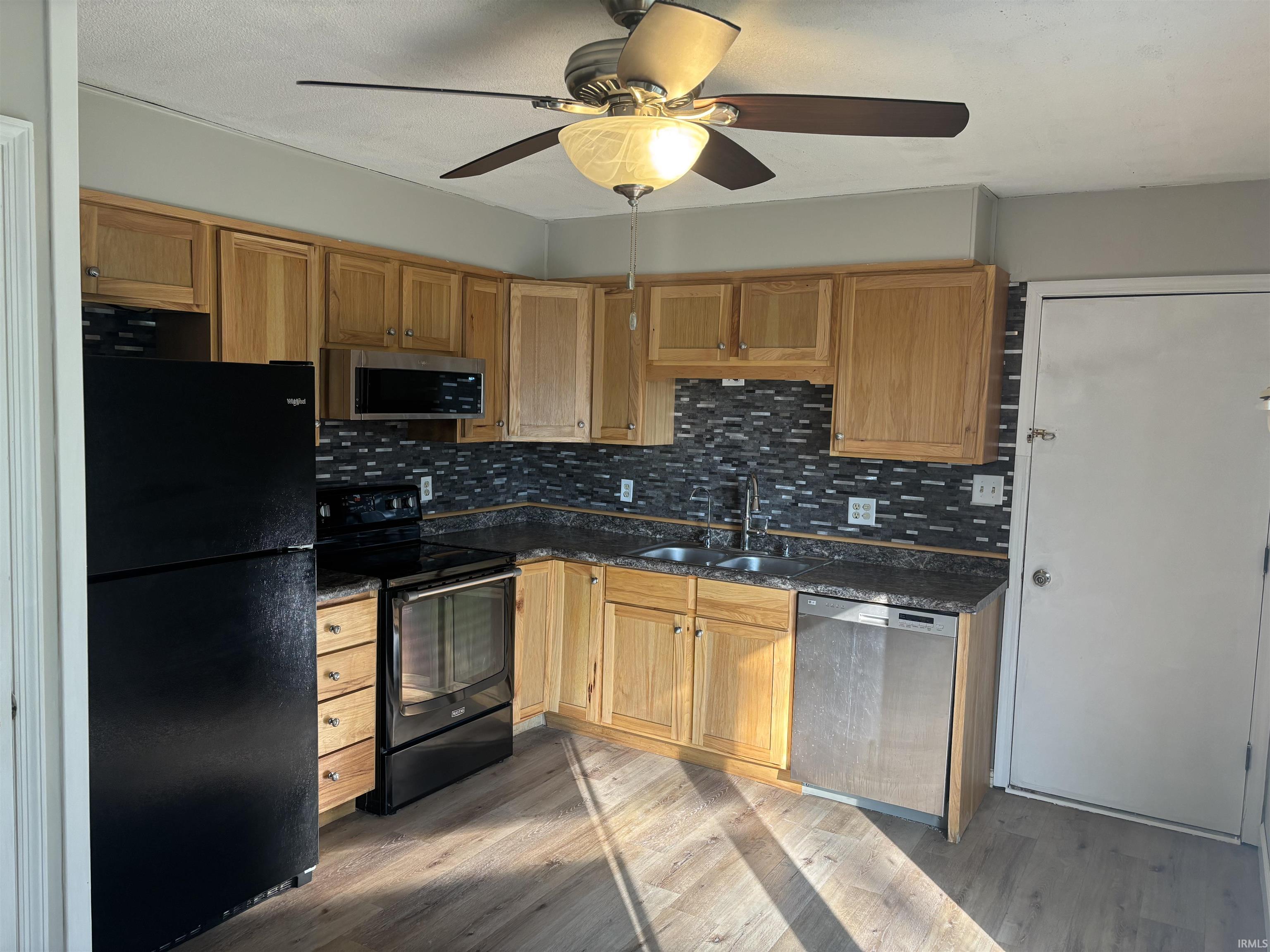 Kitchen featuring light wood cabinetry, dark speckled countertops, and a mosaic tile backsplash