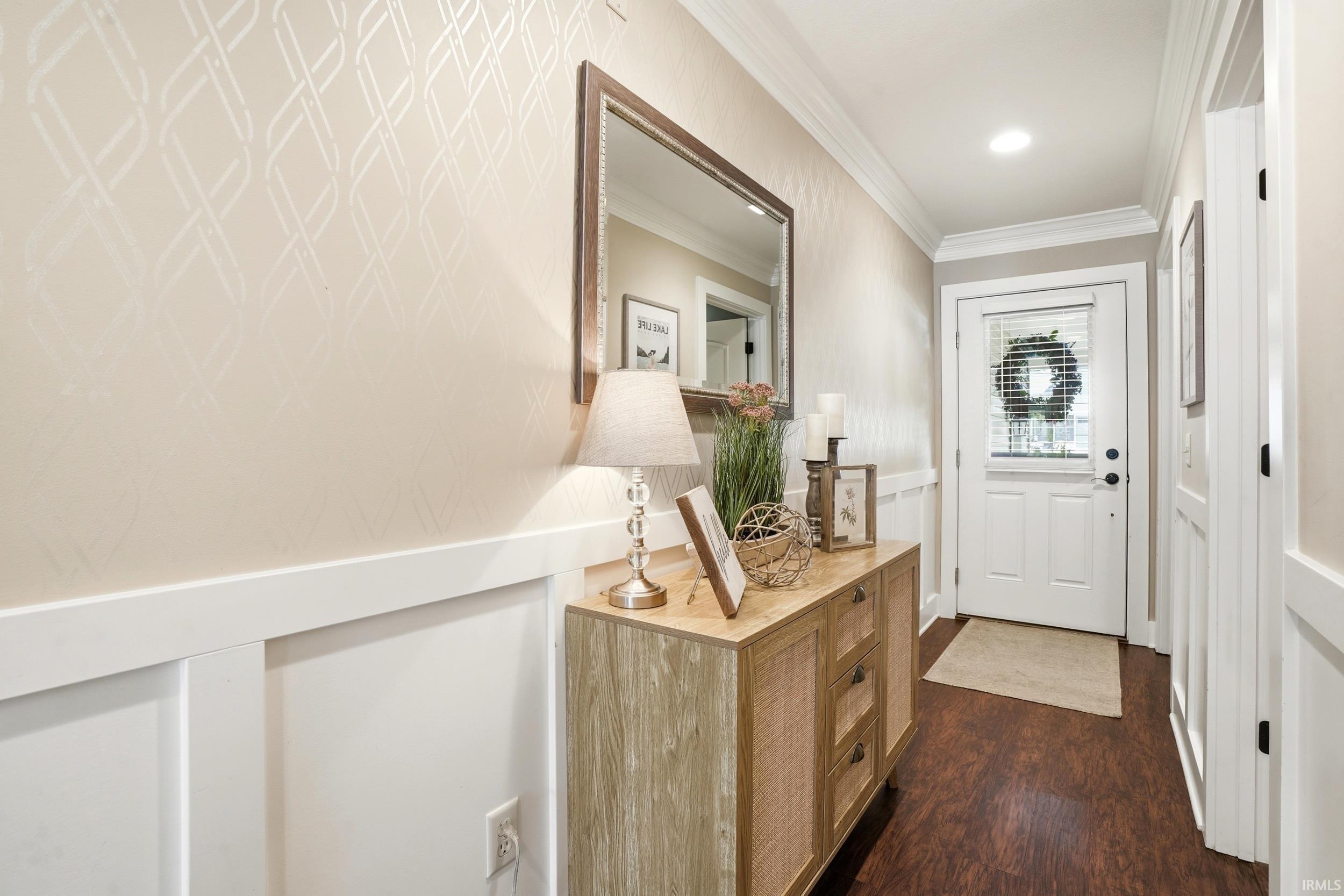 Welcoming foyer featuring wainscoting with chair rail detail, wood-finish flooring, and a framed mirror above a wood dresser