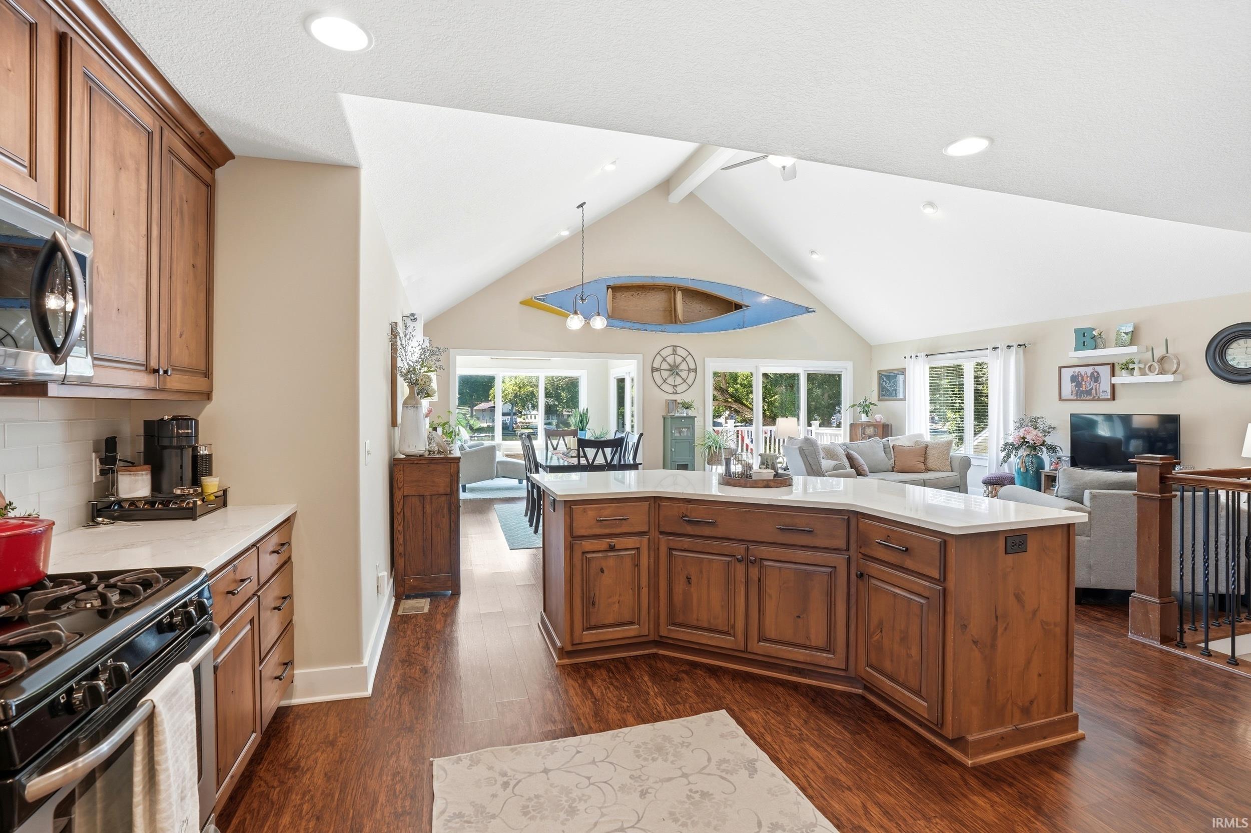 Open-concept kitchen featuring wood-finish flooring, a central island with a light-colored countertop, abundant wood cabinetry, and recessed lighting