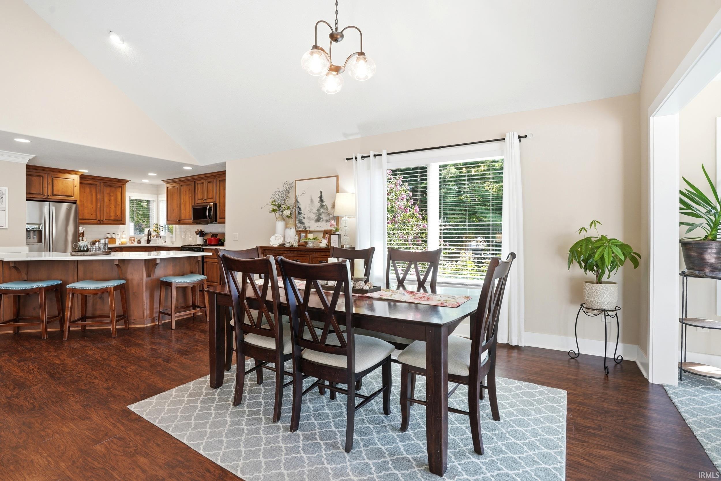 Open-concept dining and kitchen area featuring a wood-finish dining table with X-back chairs, stainless steel appliances, wood cabinetry, recessed lighting, and French doors opening to the outdoors