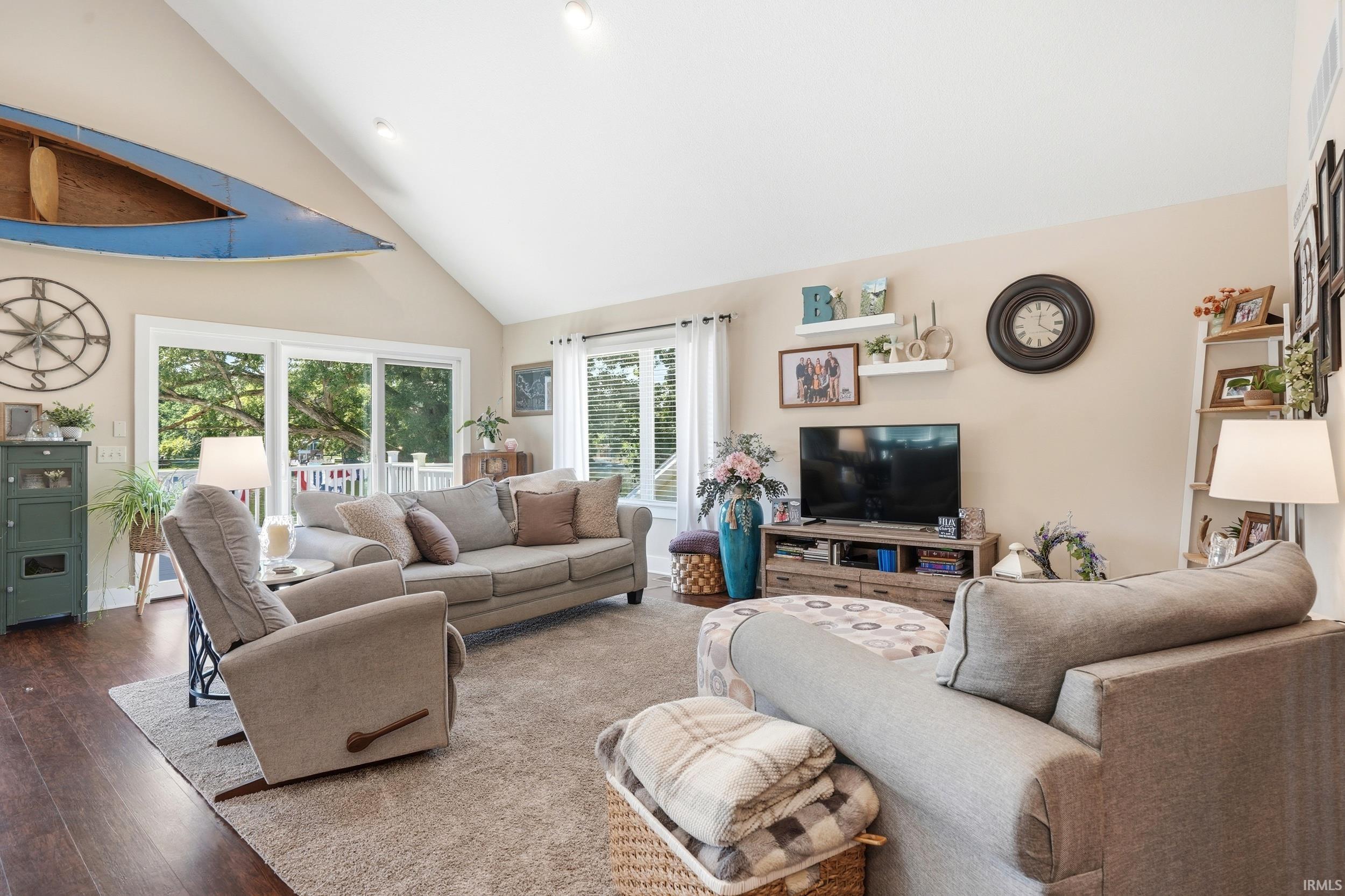 Bright, open-concept living space featuring vaulted ceilings with skylights, hardwood flooring throughout, and multiple glass doors providing natural light
