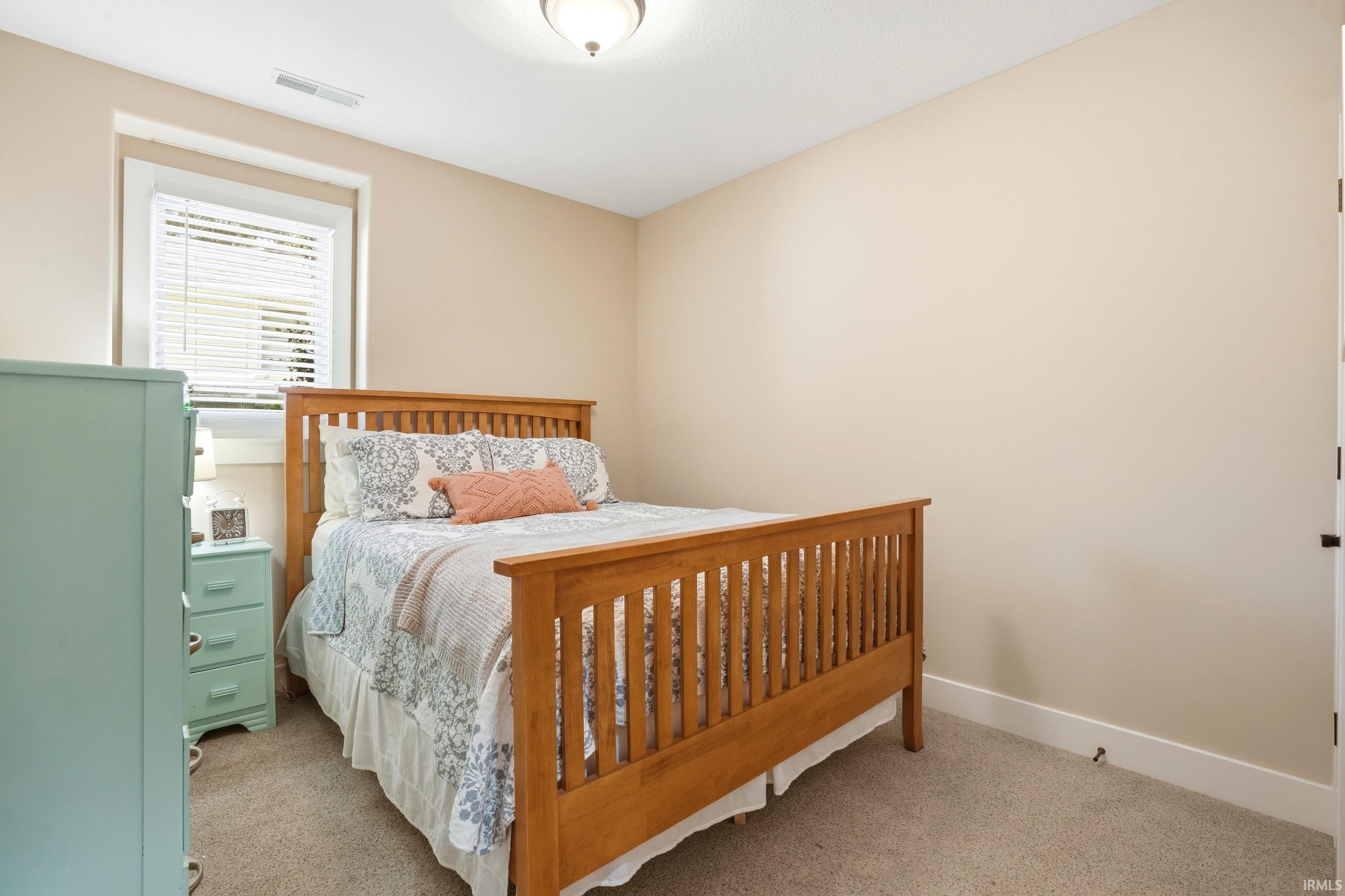 Spacious secondary bedroom featuring a solid wood bed frame with vertical slat detailing, neutral carpet flooring, and soft beige wall finishes