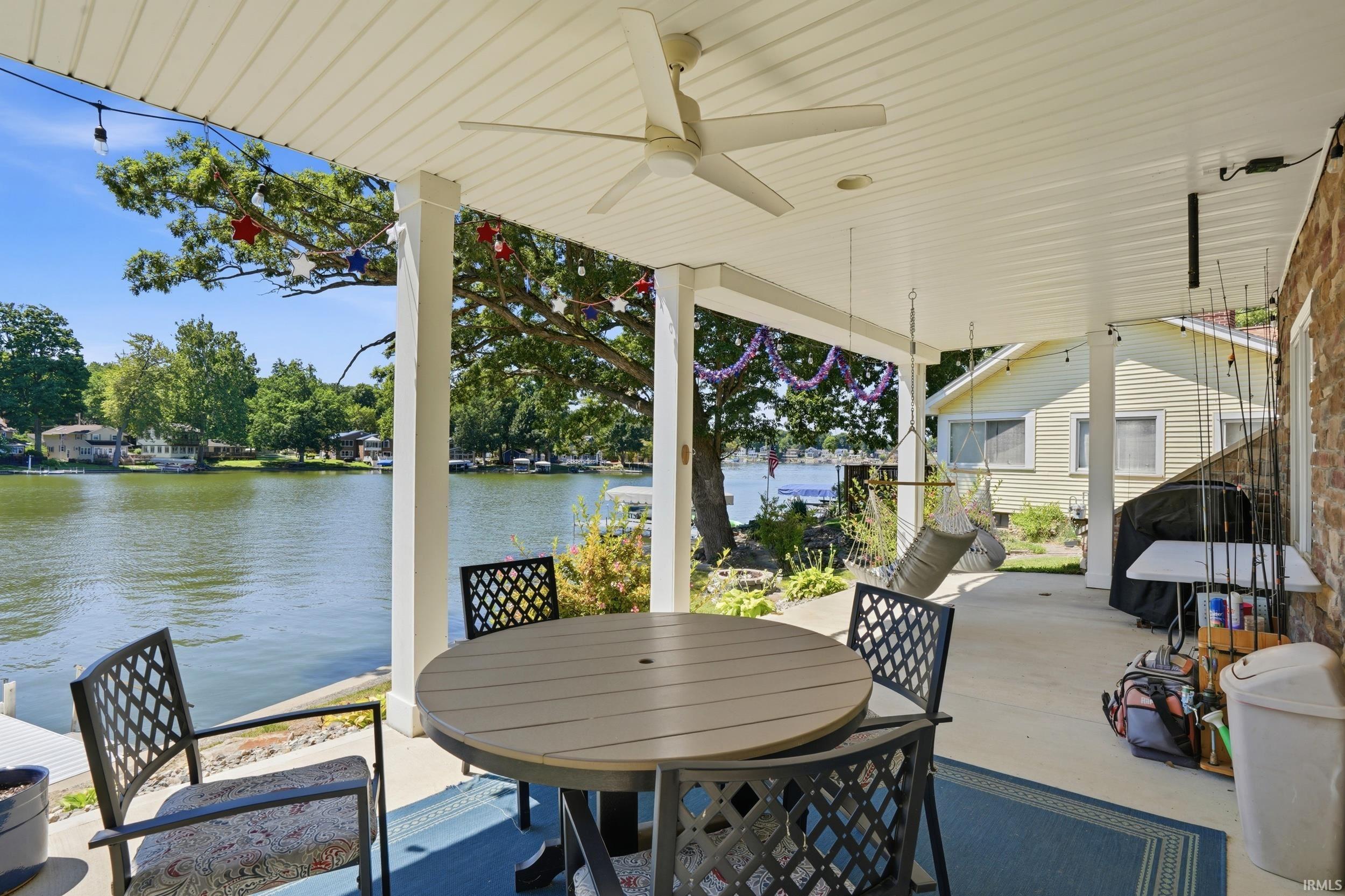 Waterfront covered porch featuring a ceiling fan, composite decking, and round dining table with lattice-back seating