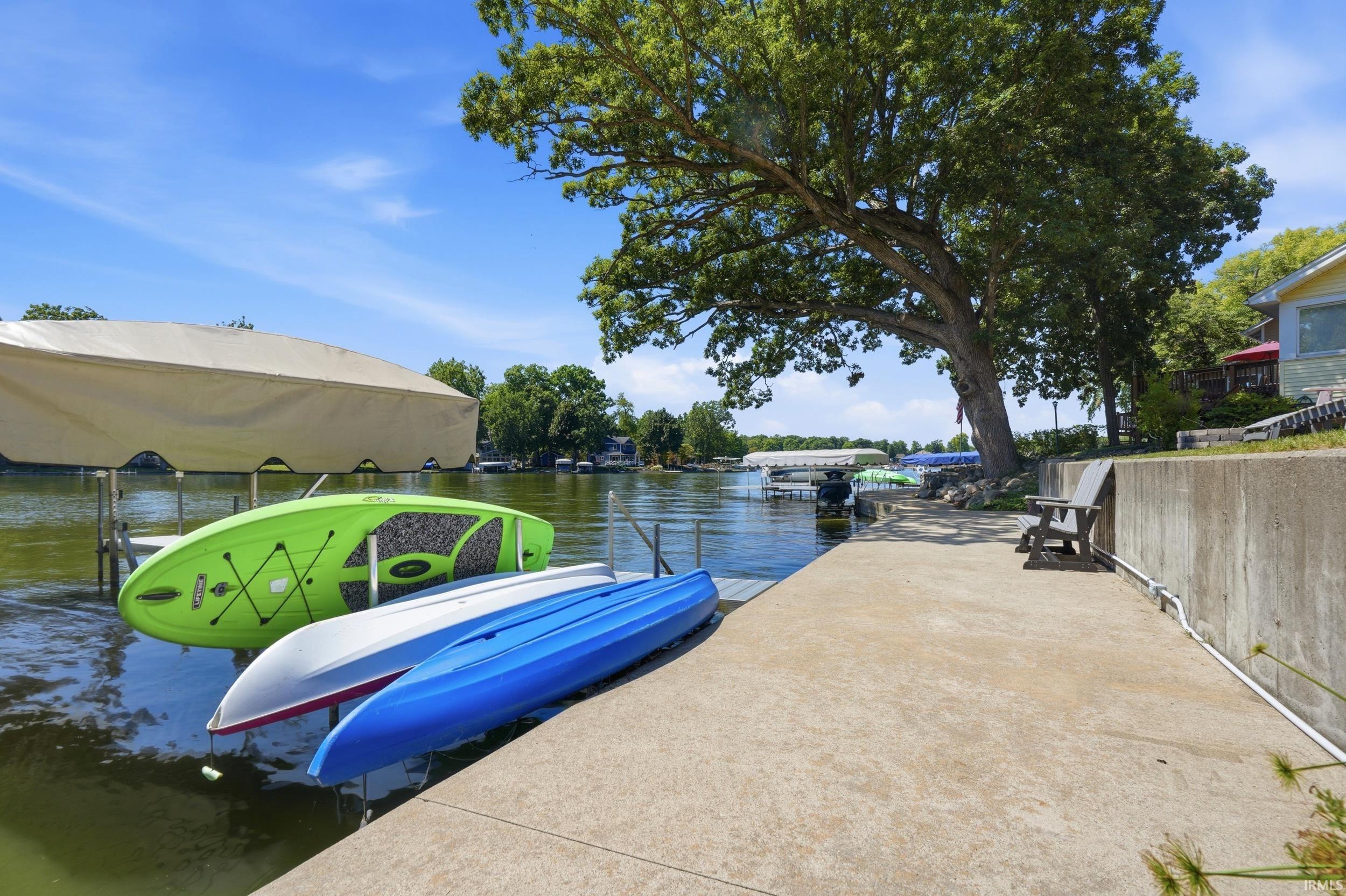 Waterfront dock featuring direct water access, concrete launch pad, mature shade trees, and moored recreational watercraft