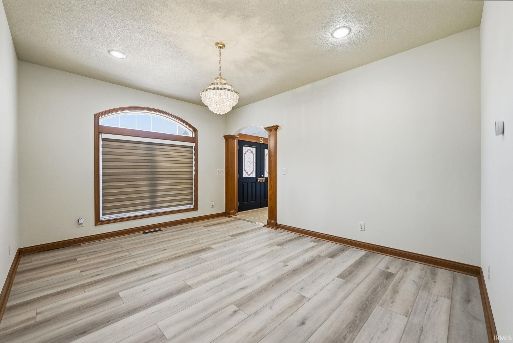 Spacious room featuring light wood-finish flooring, an arched window with integrated blinds, and recessed lighting
