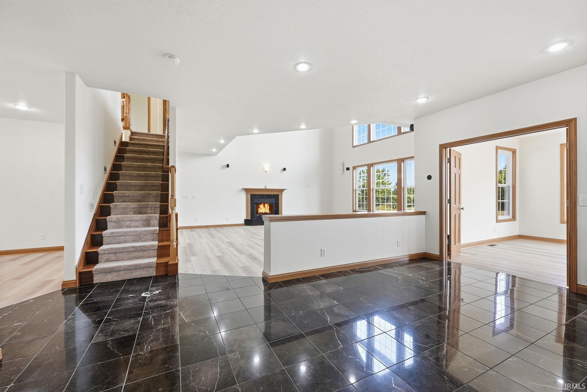 Polished black tile flooring at the entry, a carpeted staircase with wood banister, and a spacious living area featuring a fireplace with a wood mantle