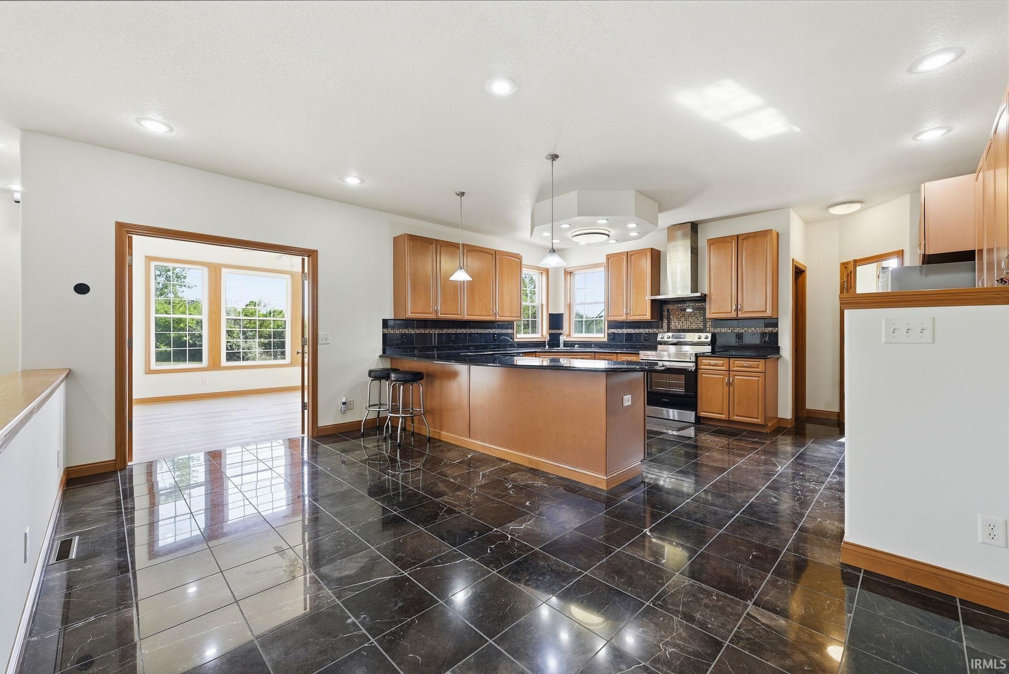 Expansive kitchen featuring dark polished tile flooring, wood cabinetry, a central island with a breakfast bar, stainless steel appliances, and recessed lighting