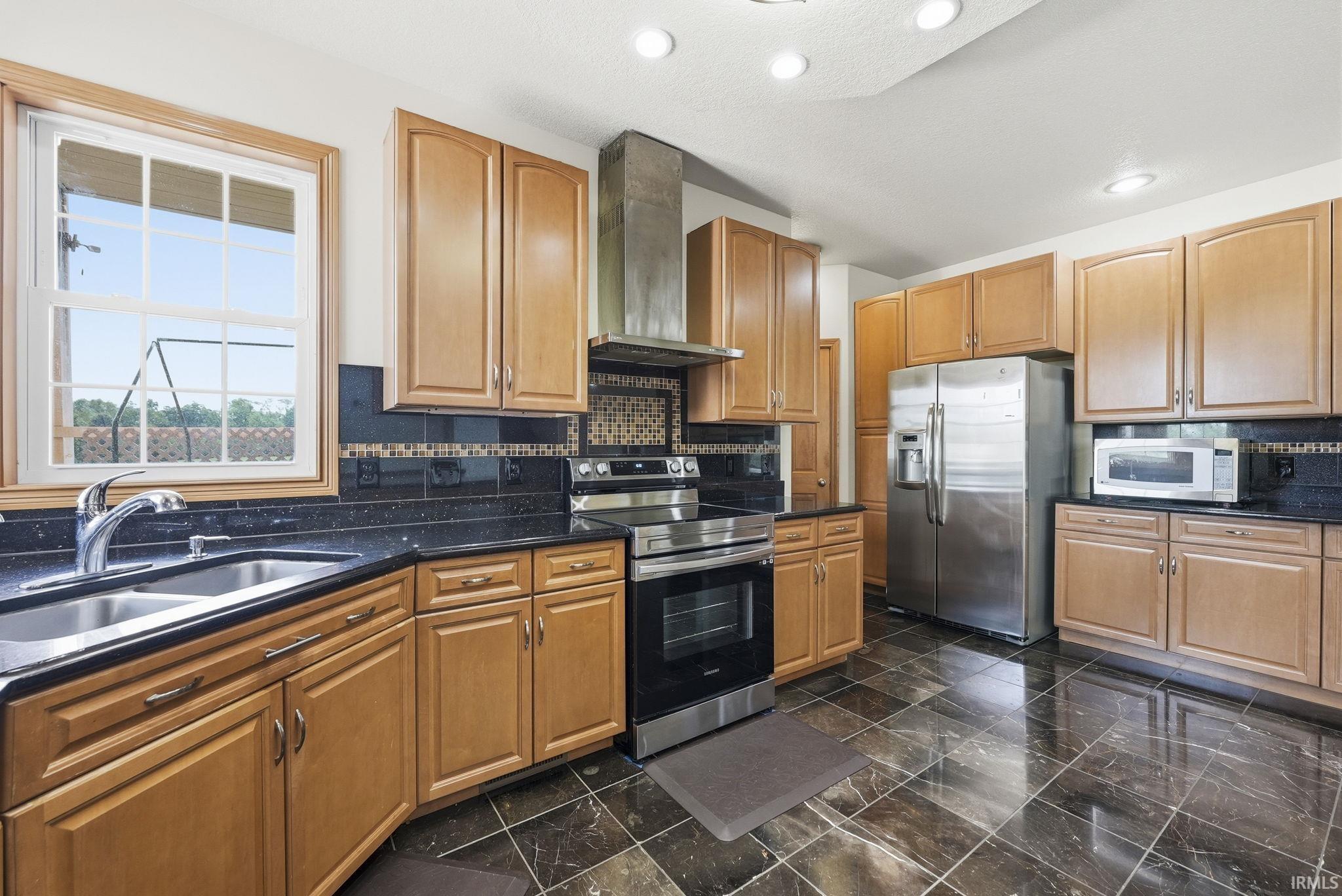 Kitchen featuring stainless steel appliances, abundant wood cabinetry, dark speckled countertops, a mosaic tile backsplash, and recessed lighting
