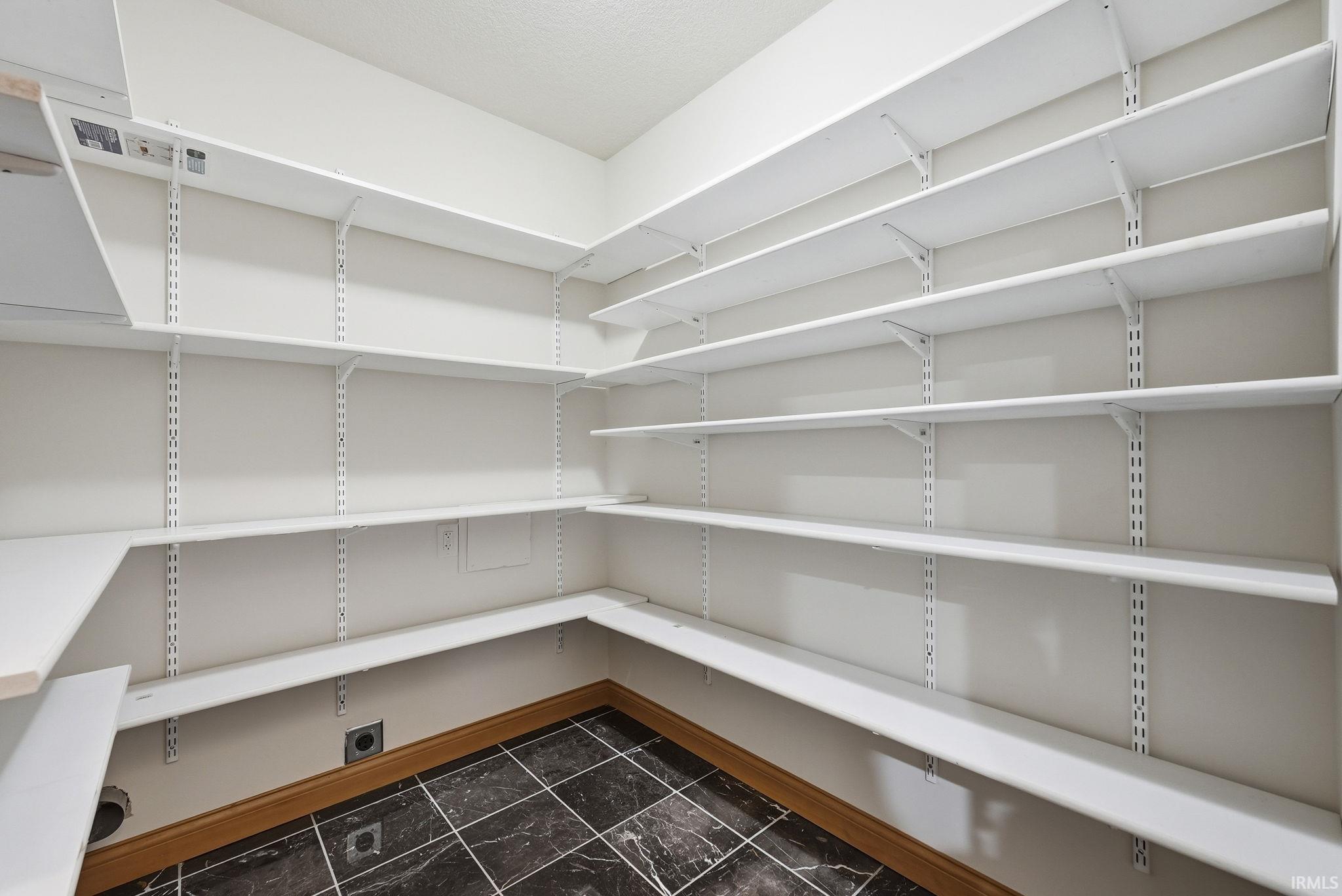 Walk-in pantry featuring extensive adjustable white shelving, dark marble-look tile flooring, and a light wood baseboard