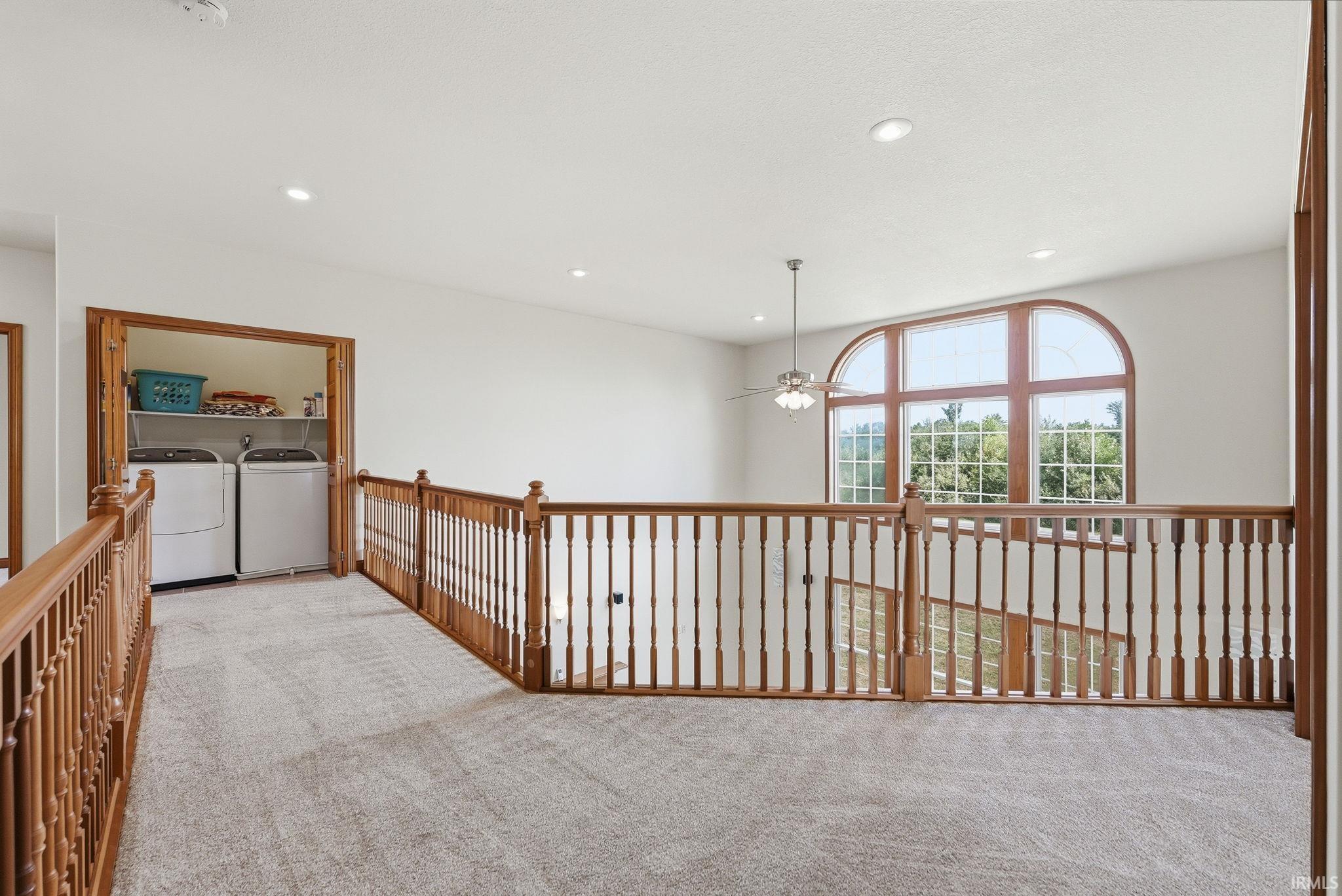 Upper-level landing featuring a large arched window, wood-finish railing, recessed lighting, and carpeted flooring