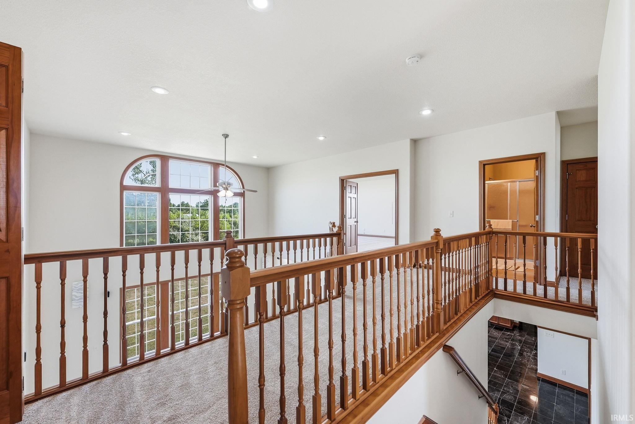 Upper-level landing featuring wood balusters and carpeting, arched window with natural light, recessed lighting, and a visible ceiling fan