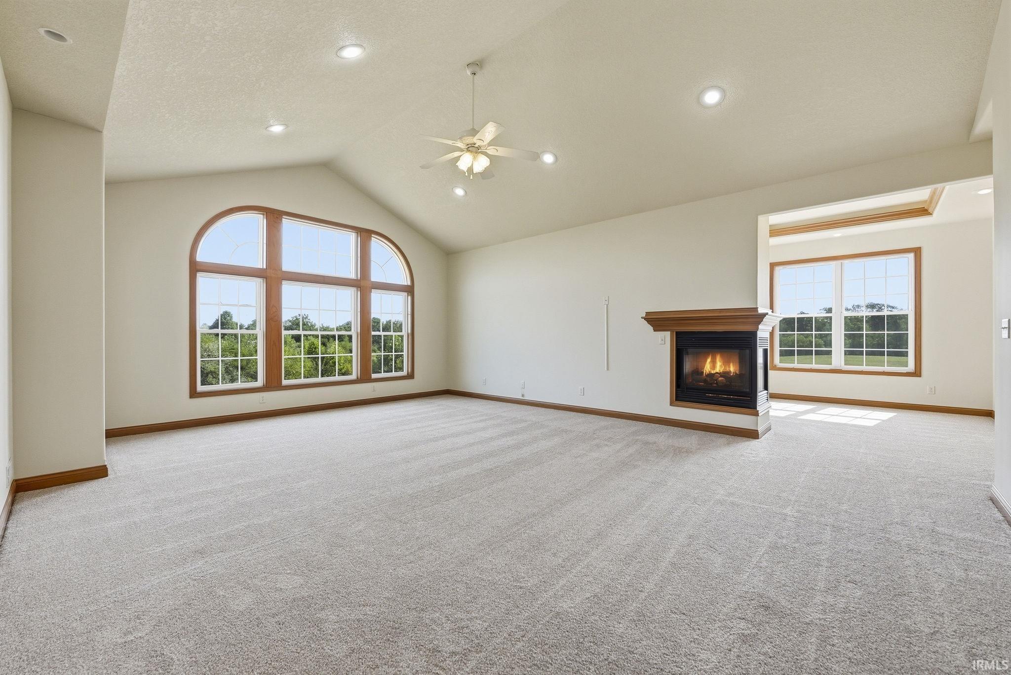 Spacious room featuring vaulted ceilings, an arched window with wood-finish trim, a gas fireplace with a wood-finish mantel, and recessed lighting