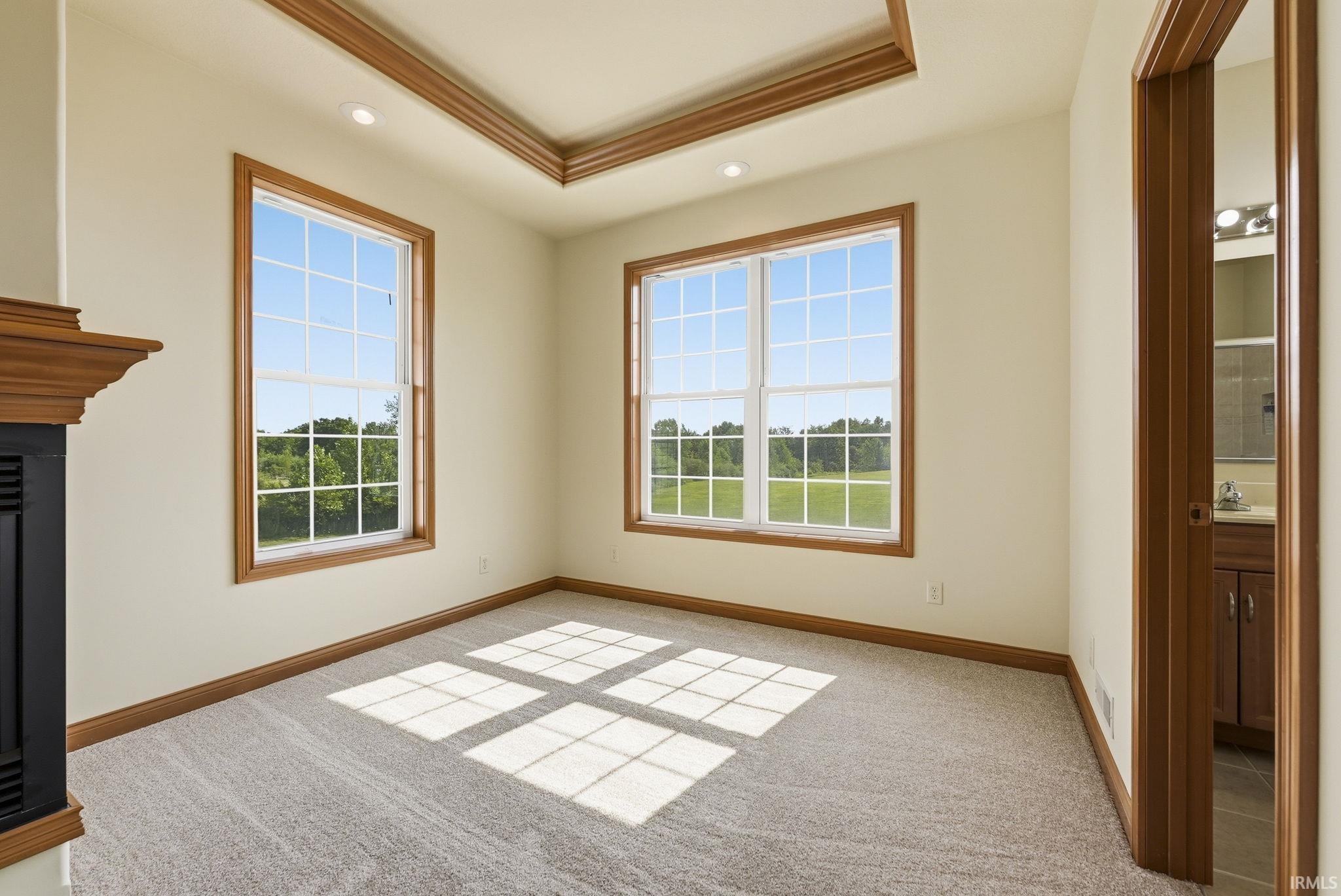 Carpeted room featuring two large windows, a tray ceiling with recessed lighting, and a fireplace with a wood mantel